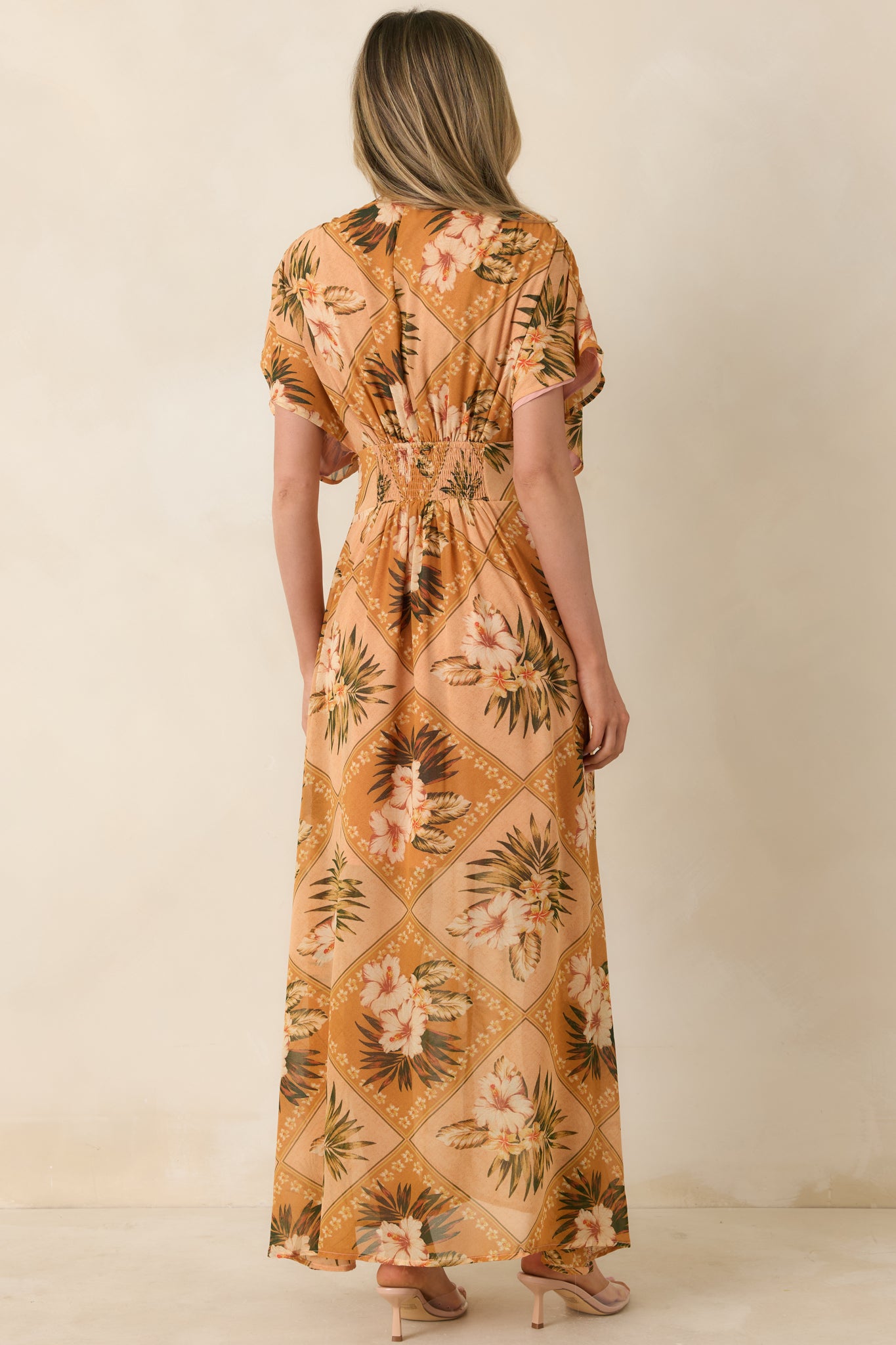 Back view of a peach multi tropical print maxi dress with flutter sleeves and flowing full-length skirt.