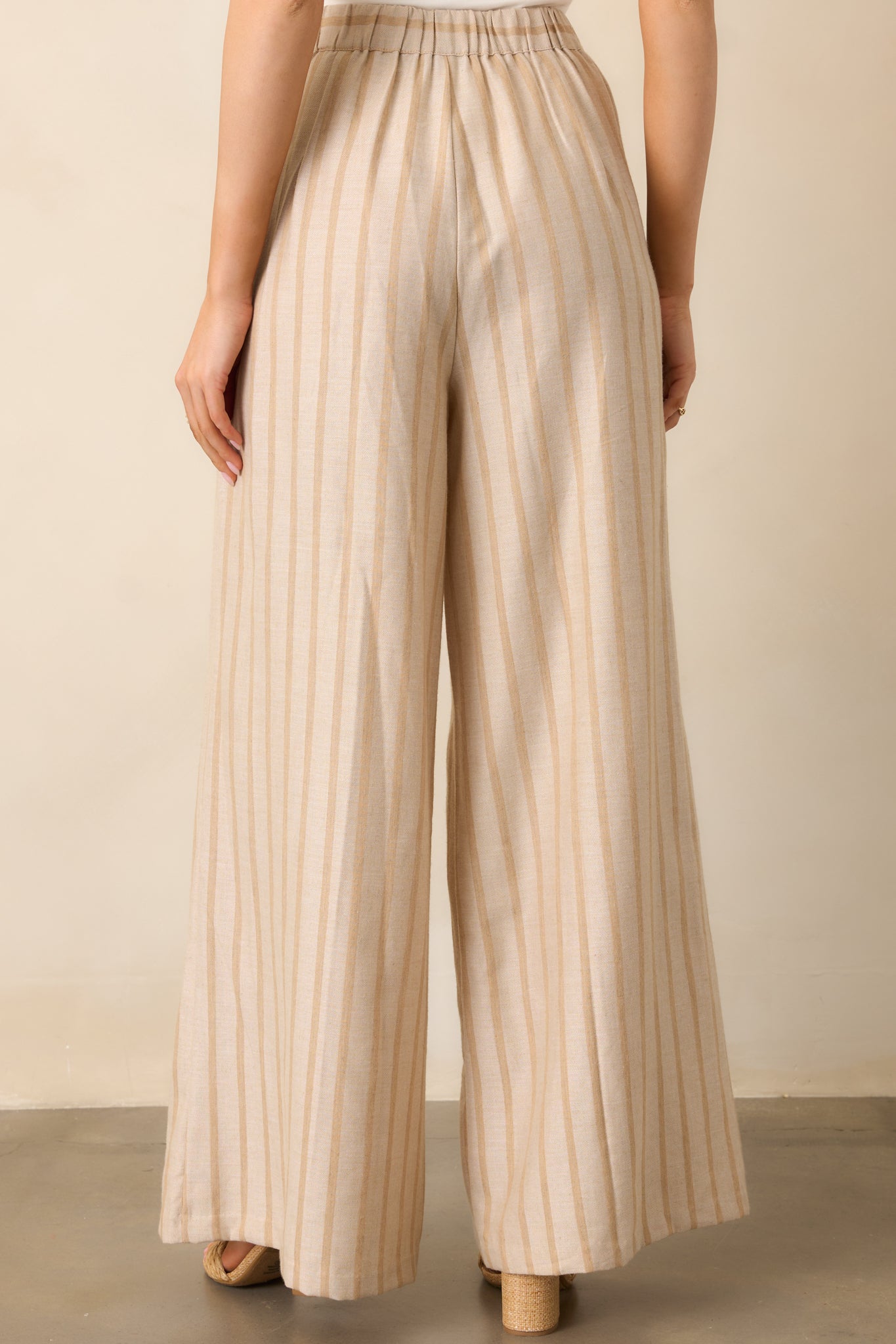 The back view of the beige pants showcasing the elastic waist insert for added comfort and the tailored wide-leg fit.