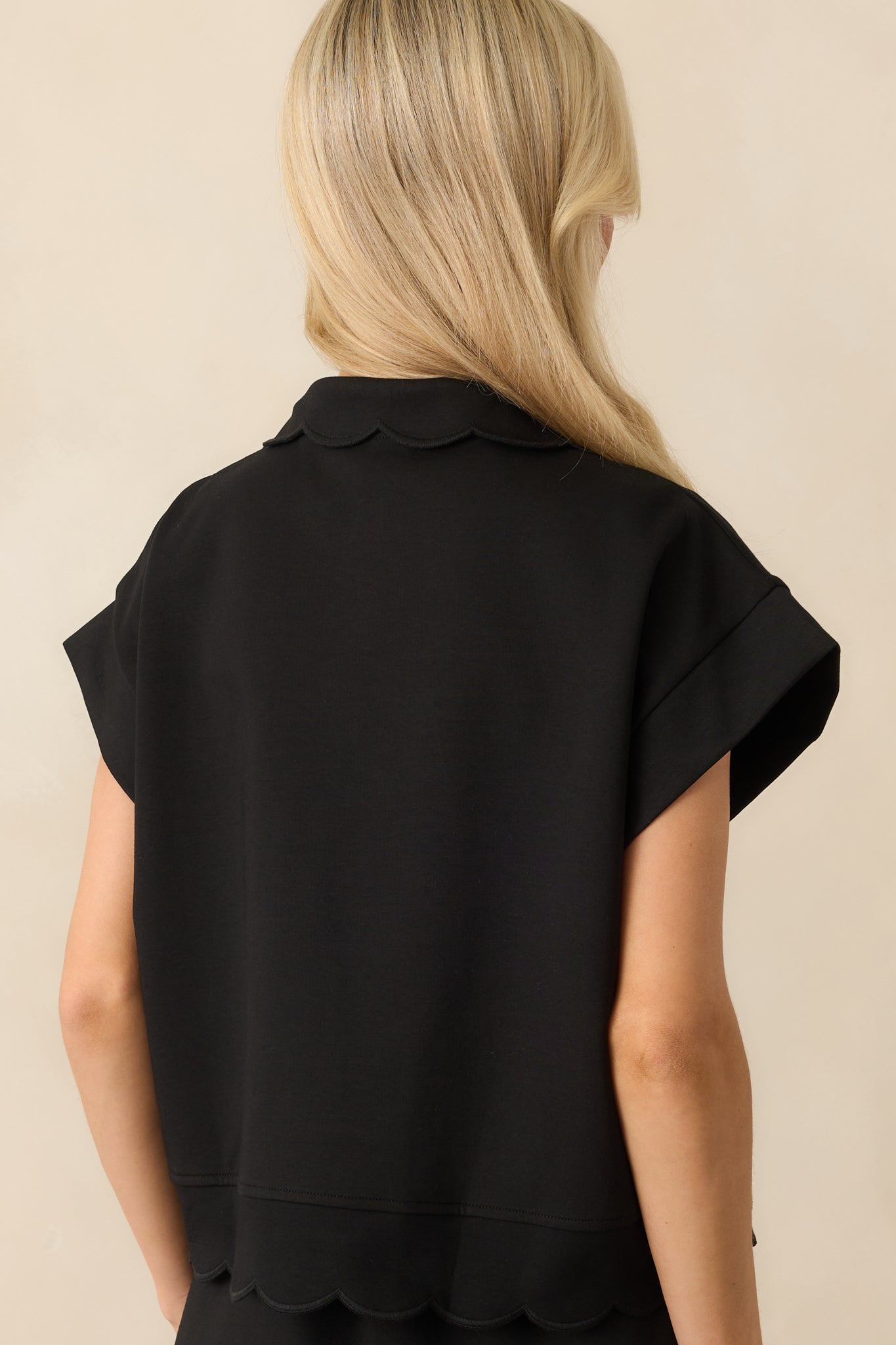 A back view of the black pullover featuring the relaxed fit and scalloped hem detail along the back hemline.