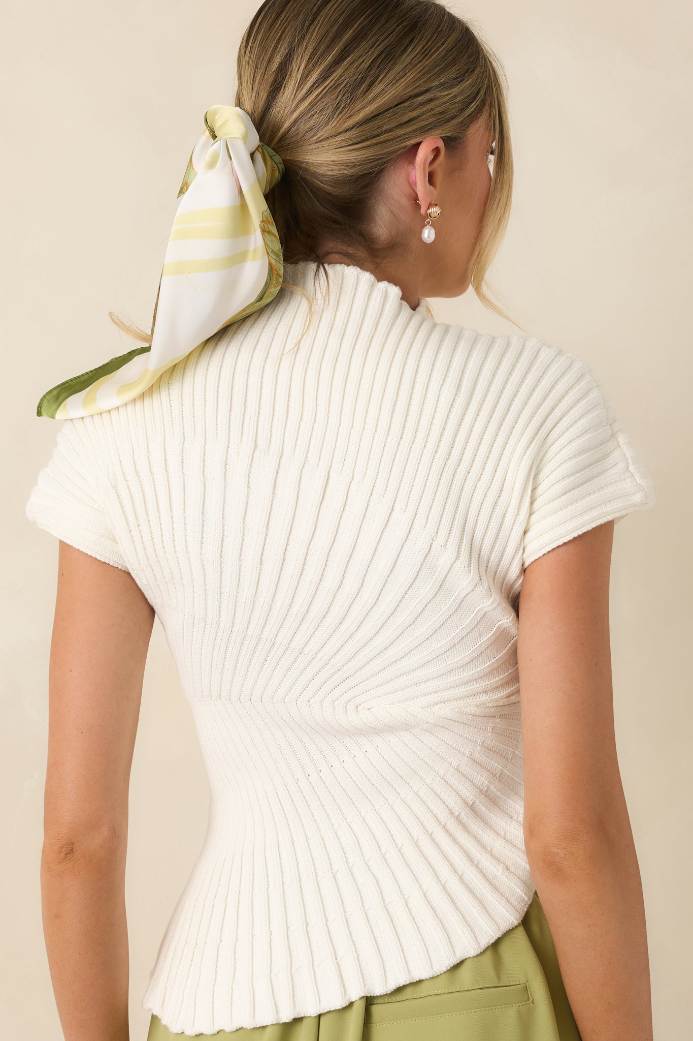Back view of the white ribbed knit top highlighting the fitted silhouette, cap sleeves, and asymmetrical hem design.