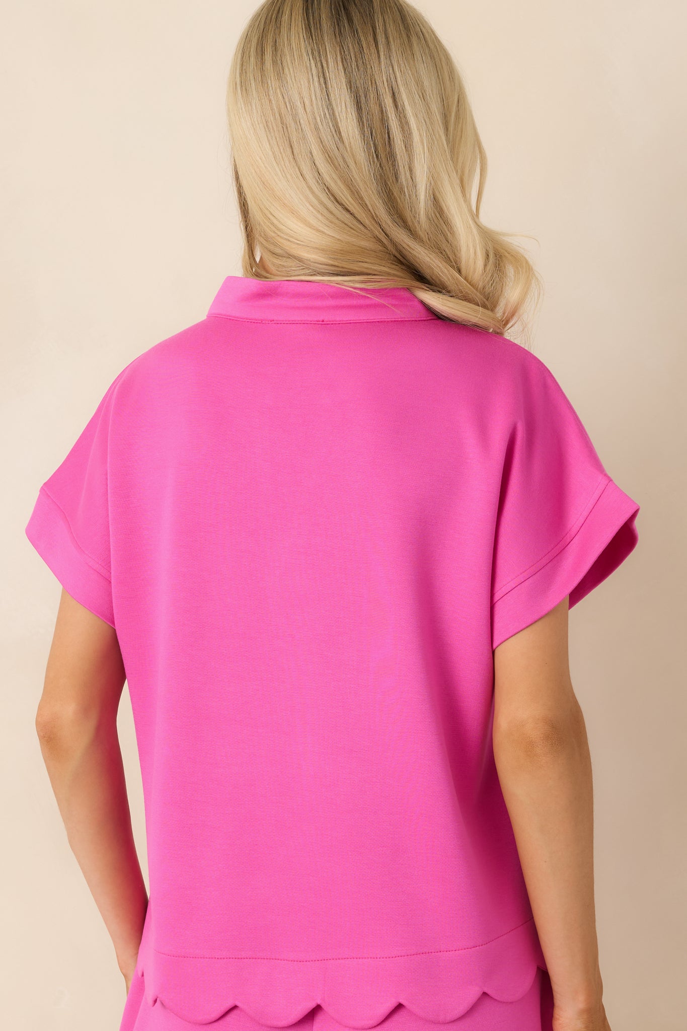 Back view of the hot pink top highlighting the relaxed silhouette, short sleeves, and scalloped hemline.