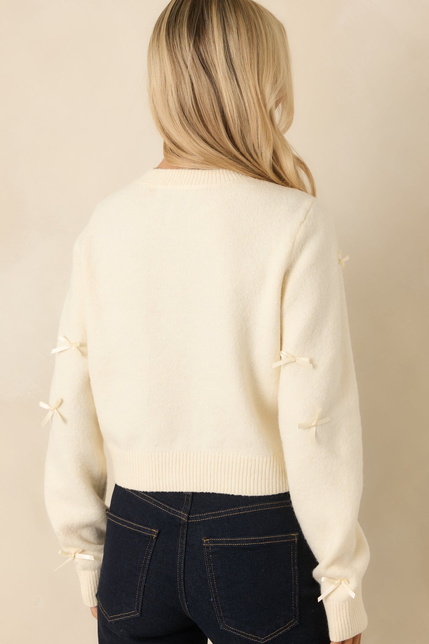 Back view of the ivory knit cardigan highlighting the slightly fitted silhouette and ribbed hemline.
