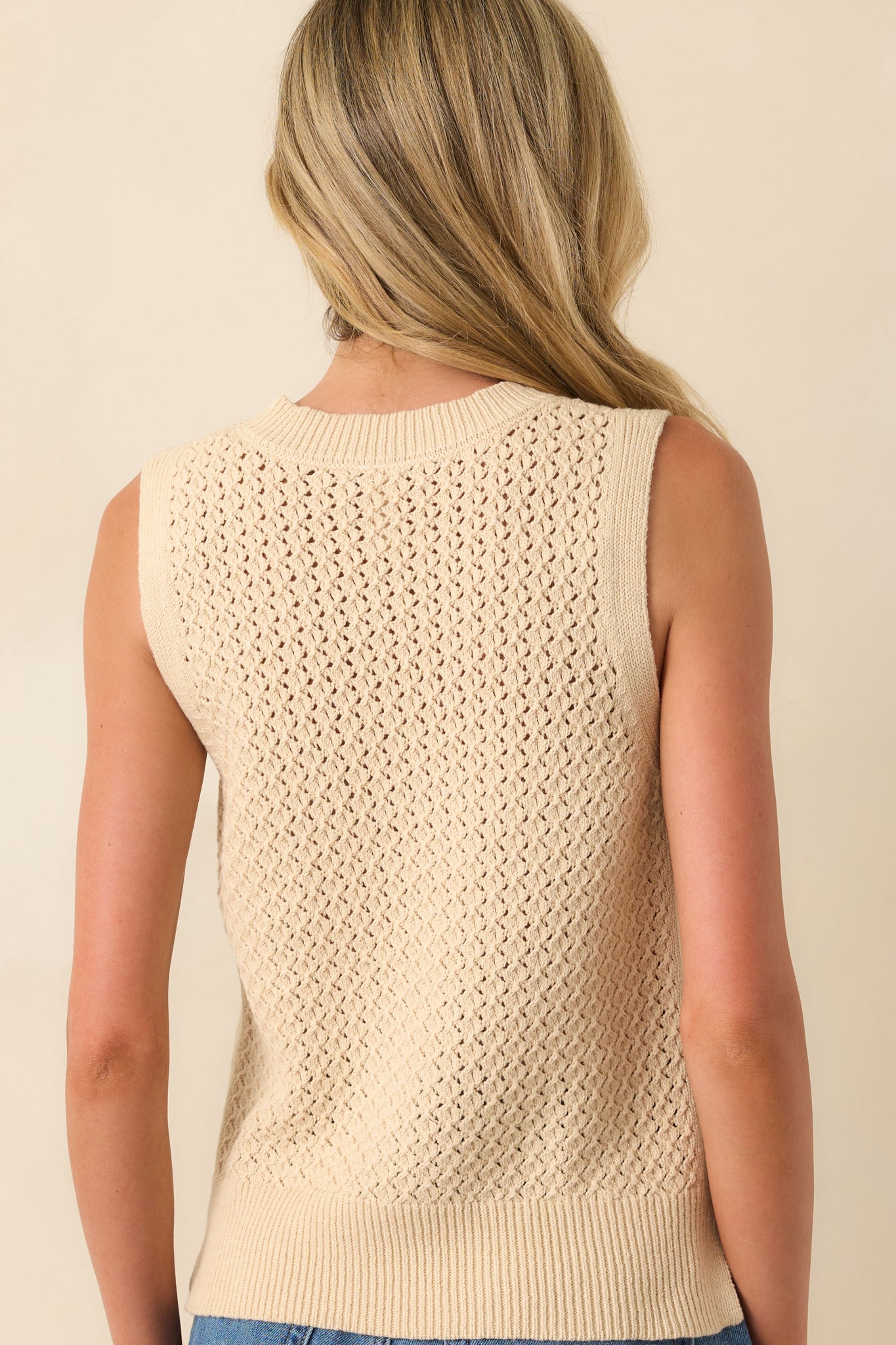A back view of the beige top highlighting the continuation of the open knit design and ribbed hem.