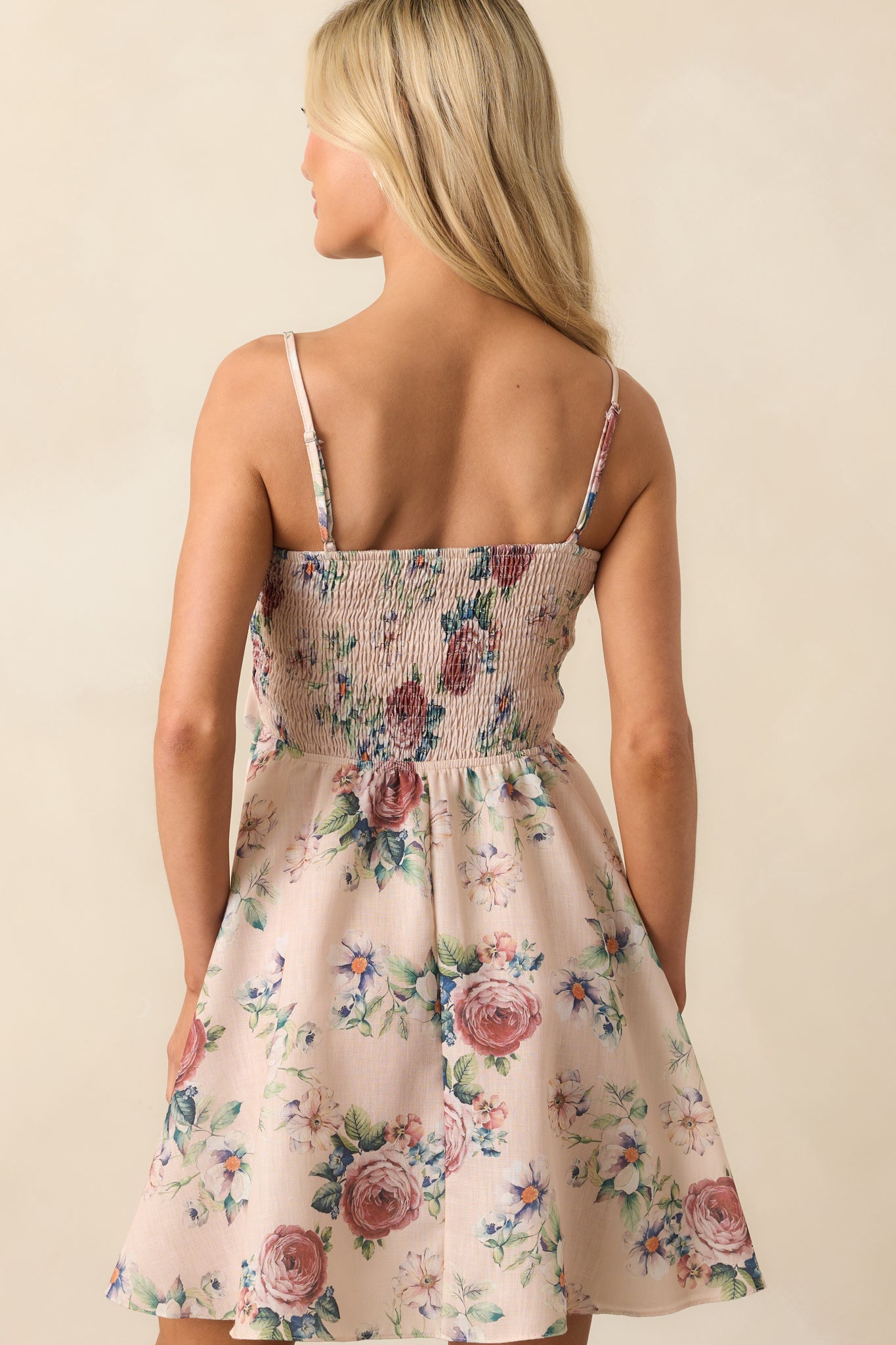 Back view of the beige mini dress, emphasizing the smocked back panel and adjustable straps.