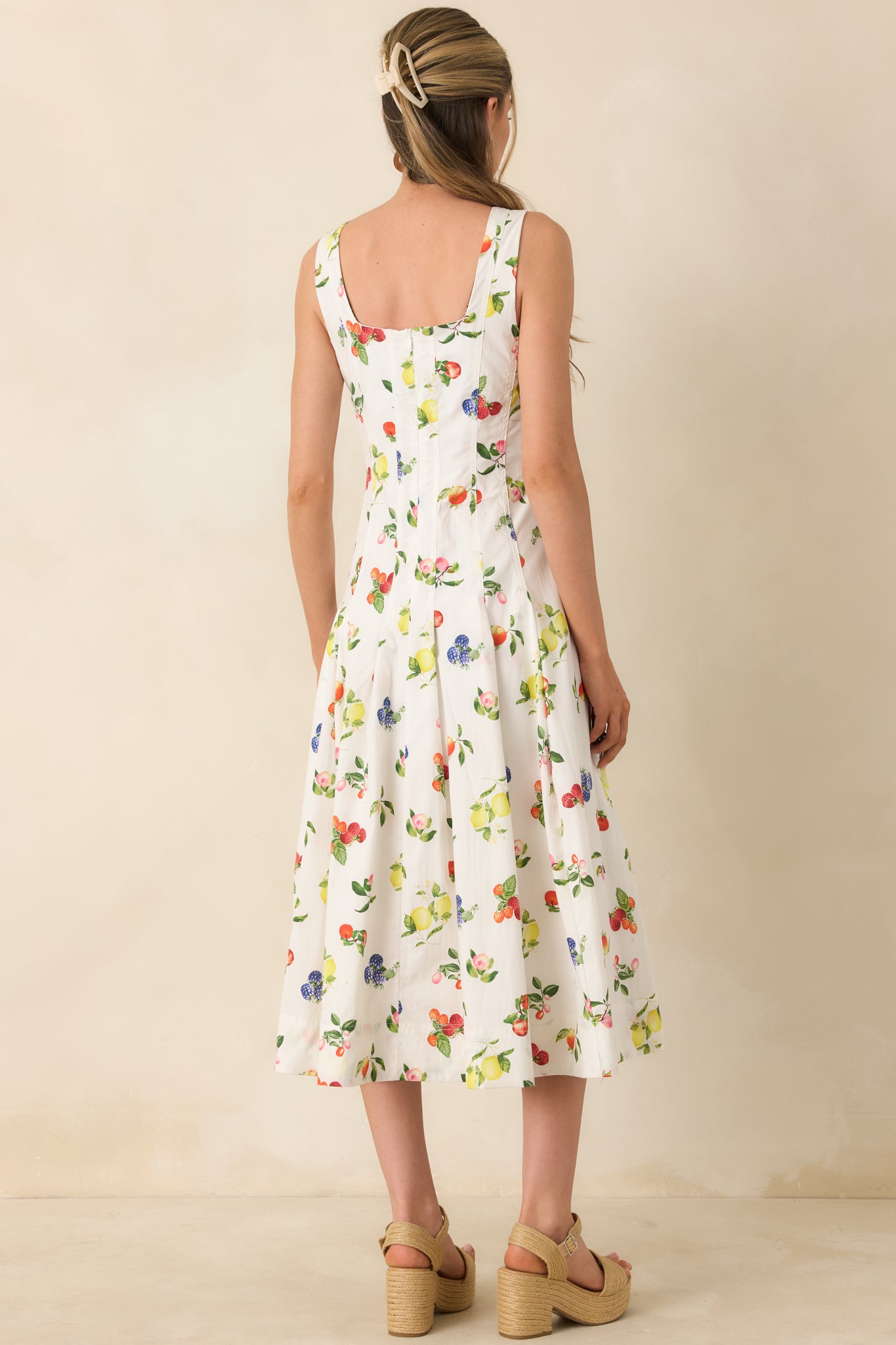 Back view of white cotton midi dress with zip-up closure, pleated skirt, and allover fruit print