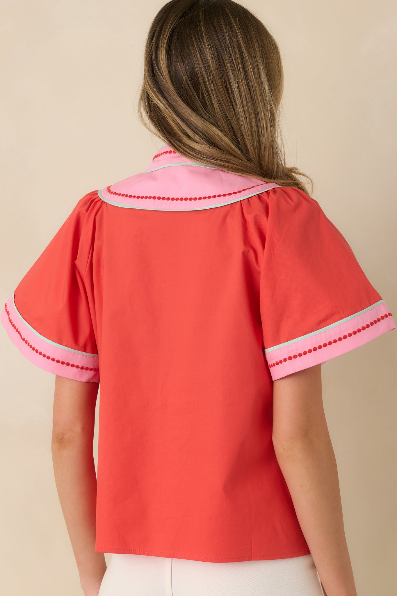 Back view of the orange-red cotton top highlighting the smooth fabric, short sleeves, and relaxed fit.