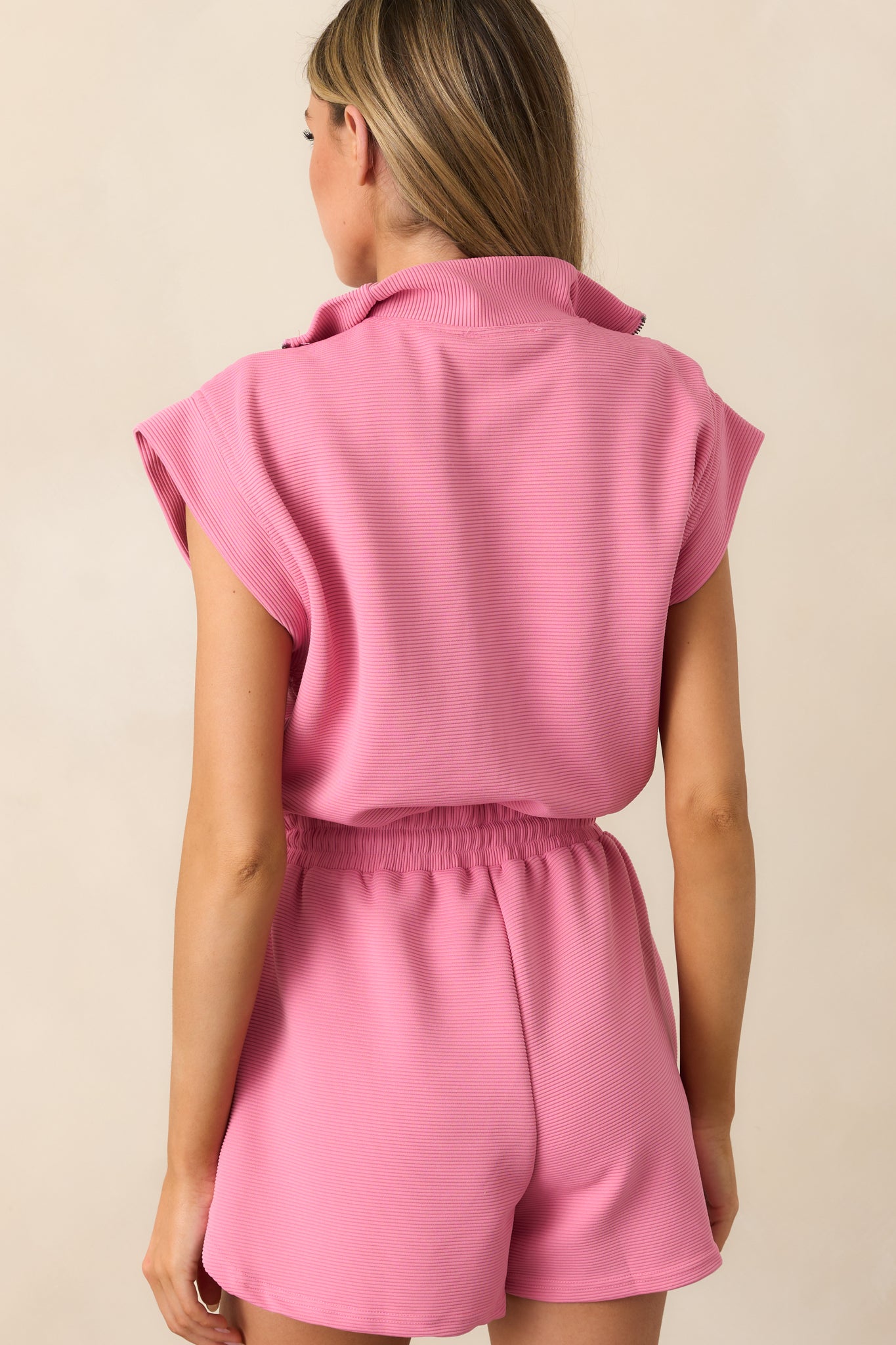 The back of the pink romper, showing the smooth ribbed texture, cap sleeves, and zip closure details.