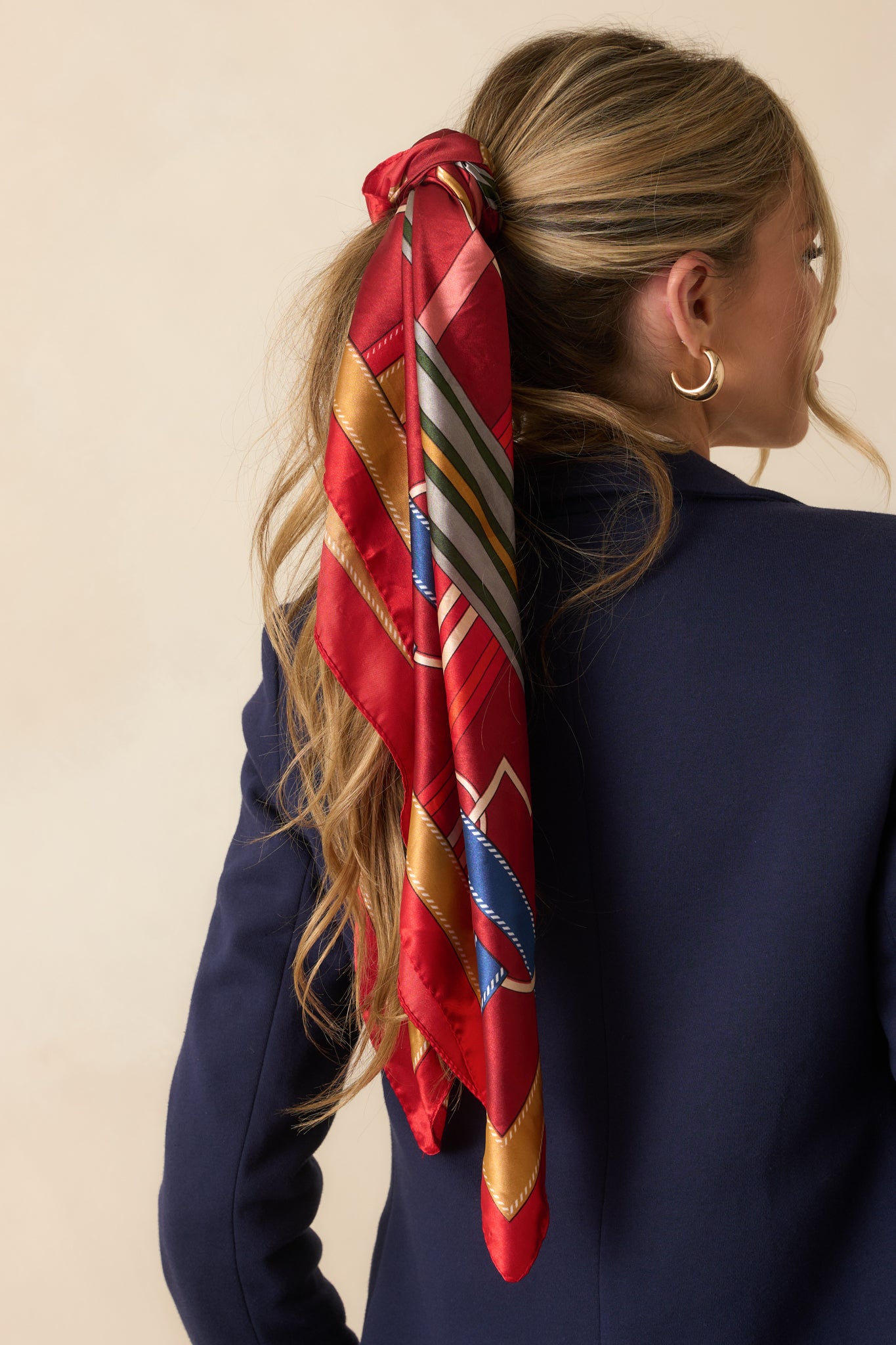 A back view of the red satin scarf being worn, highlighting its multicolored design visible across the draped fabric.
