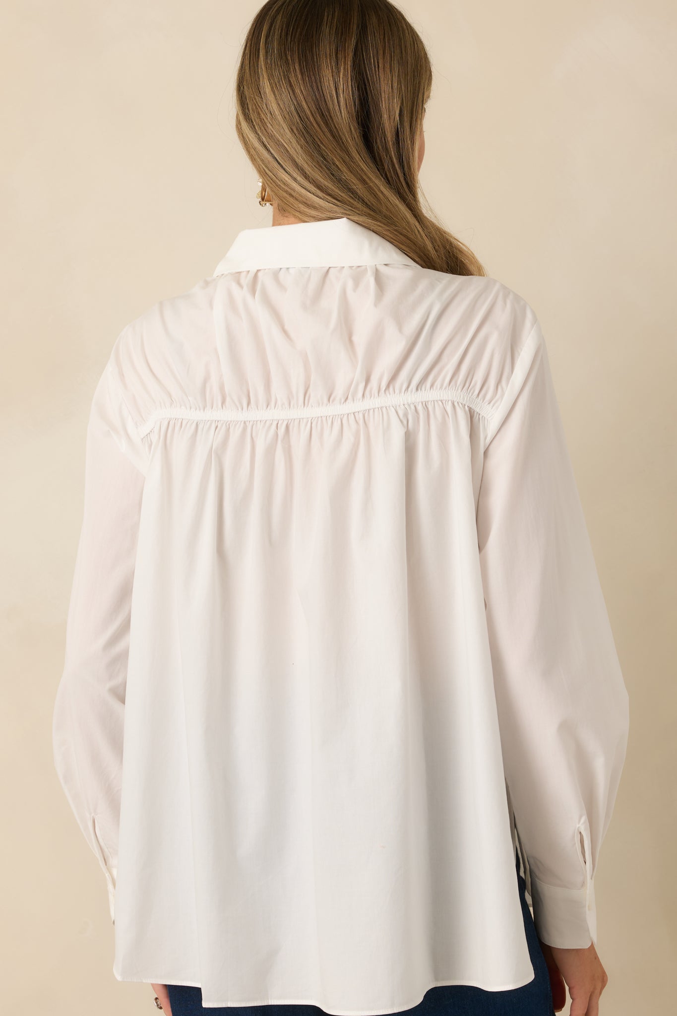 Back view of white woven blouse with relaxed fit and long sleeves, showing smooth lightweight fabric without embellishment.