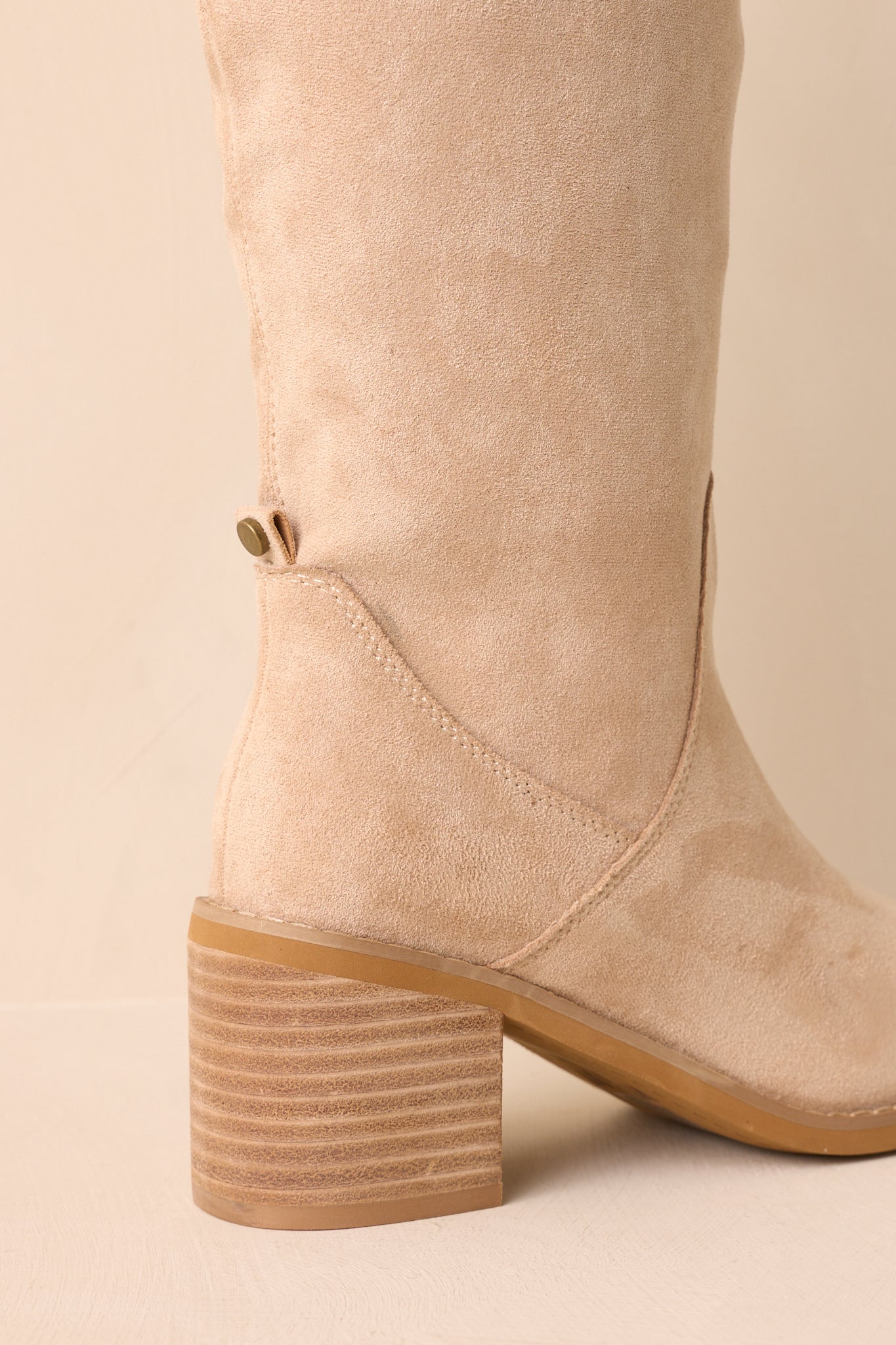 Back view of beige knee-high boots showing pull tabs, stacked block heel, and smooth faux suede finish.