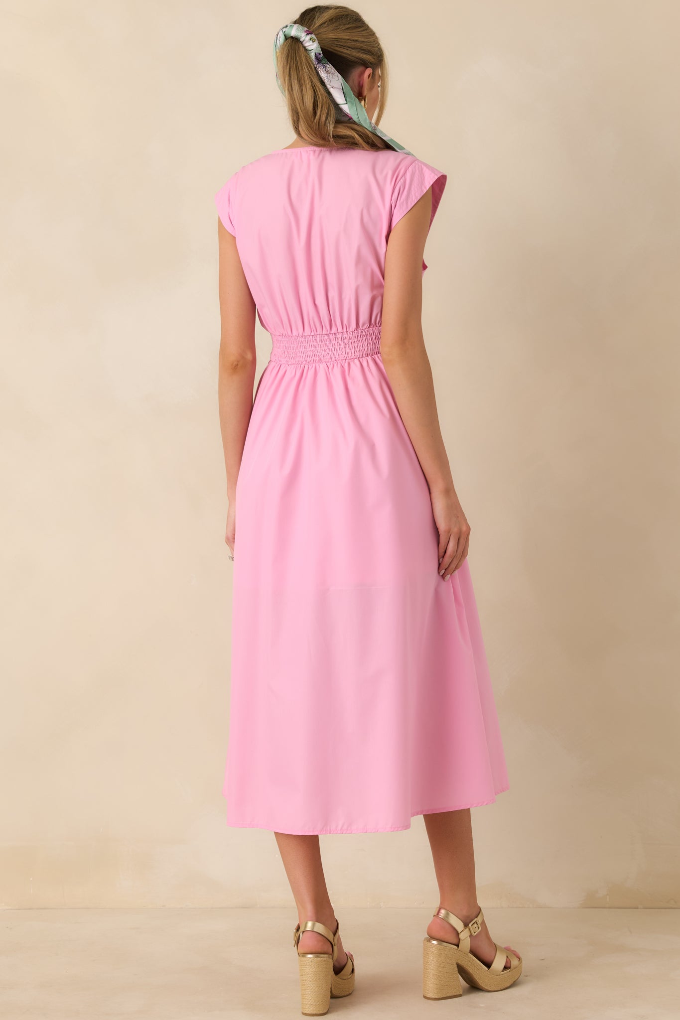 Back view of the pink midi dress showing the sleeveless silhouette, fitted waist shaping, and softly gathered skirt at midi length.