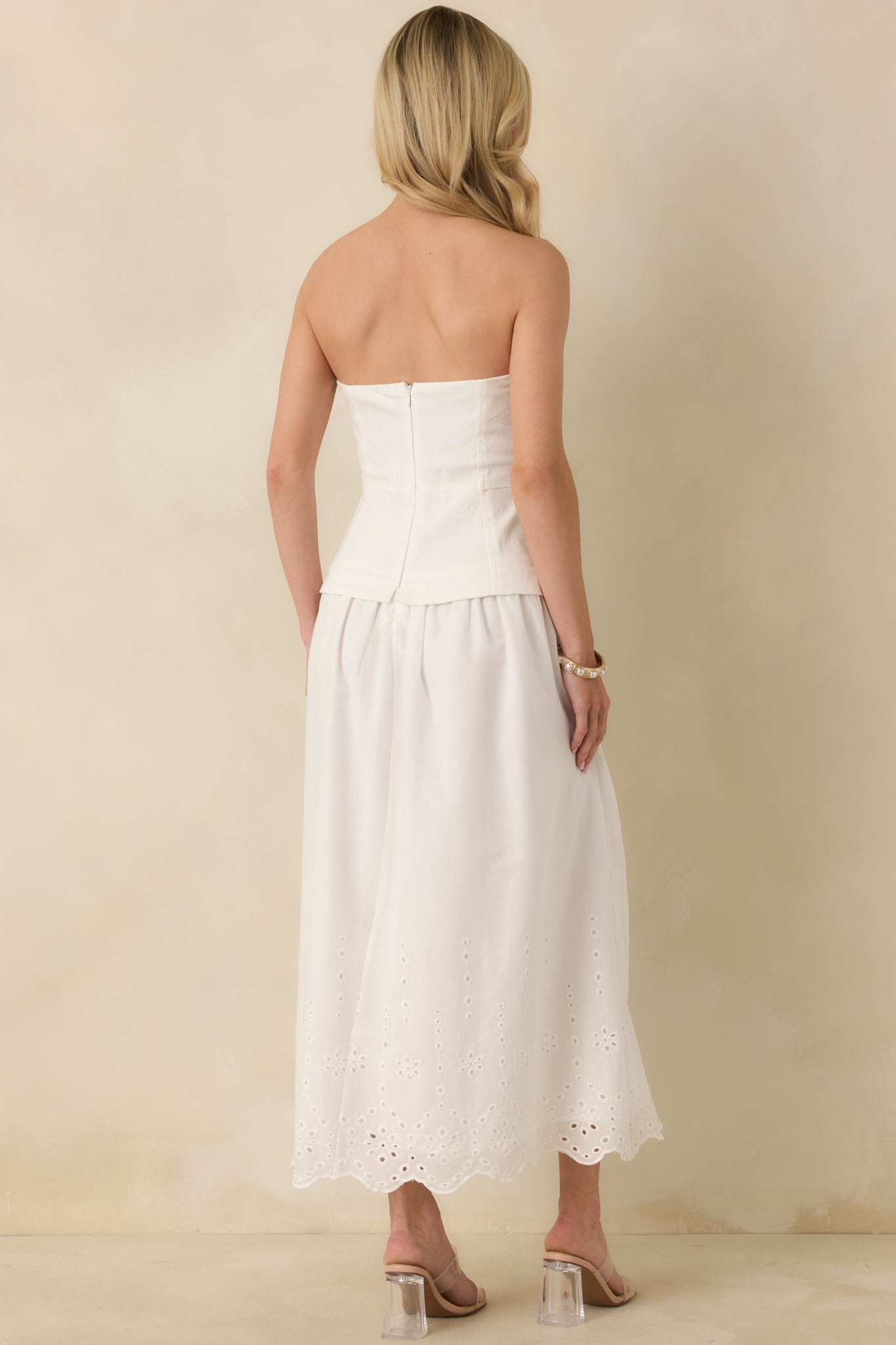 Back view of the white strapless midi dress showing the smooth structured bodice, defined waist seam, and flowing skirt with eyelet lace trim at the hem.