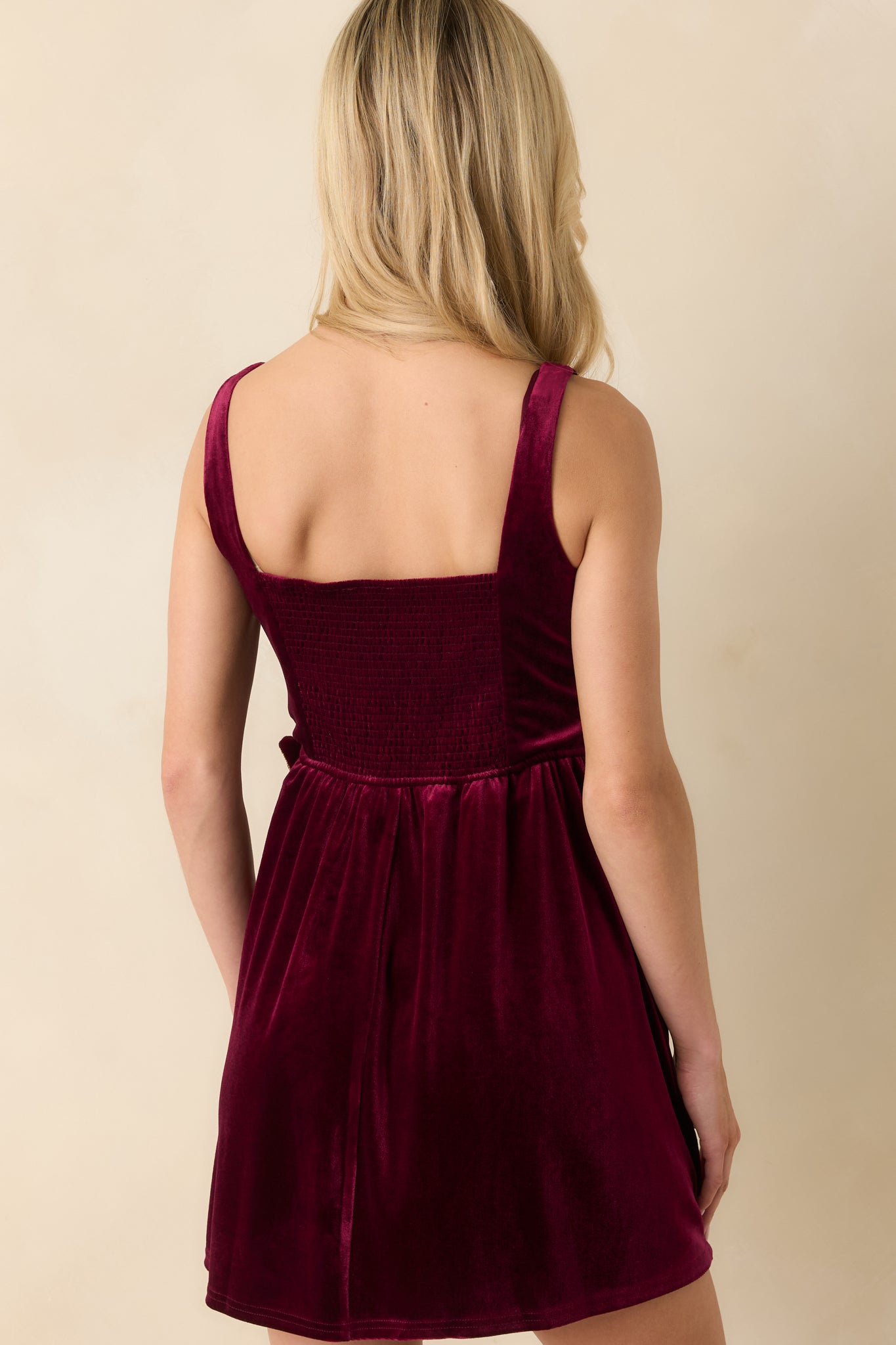 Back view showing smocked panel, fitted bodice, and flared skirt of the burgundy velvet mini dress.