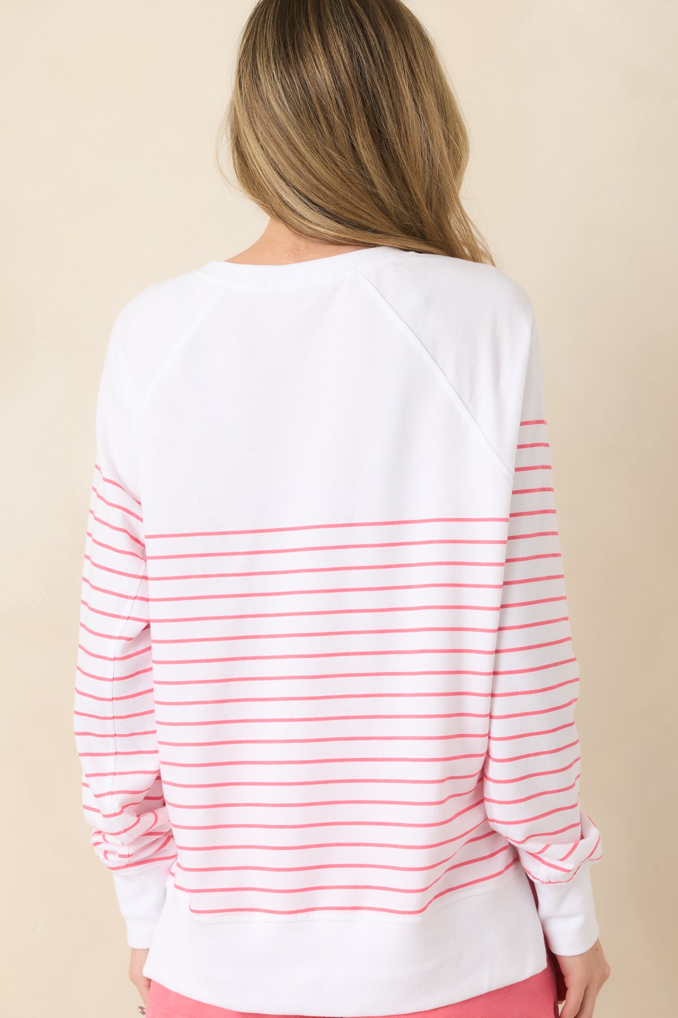 Back view of white oversized pullover displaying raglan sleeves, horizontal stripe design, and ribbed hem.
