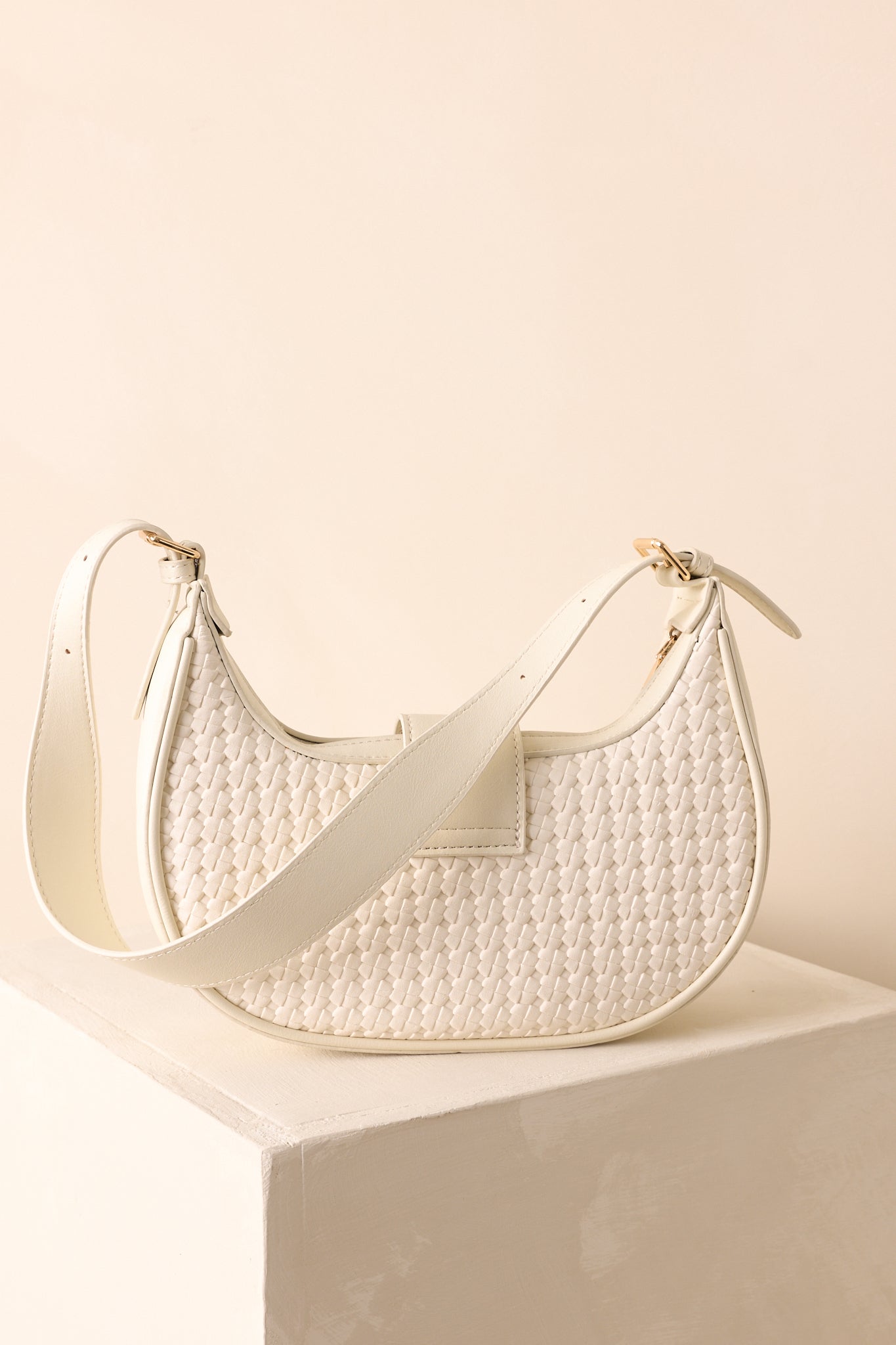 A back view of the shoulder bag featuring a smooth woven design and curved half-moon shape.