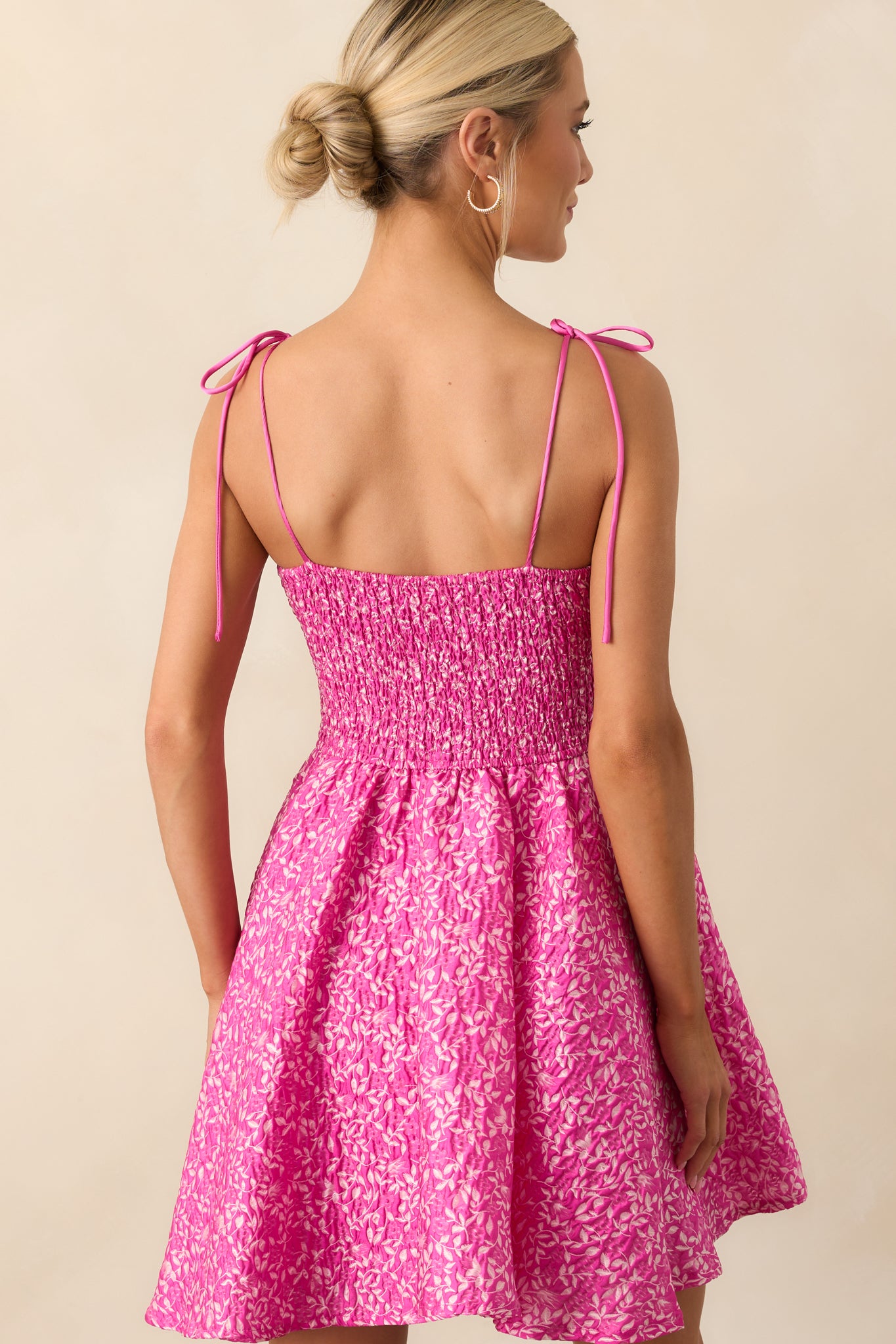 A view from behind showing the smocked panel and tied bow straps of the floral mini dress.