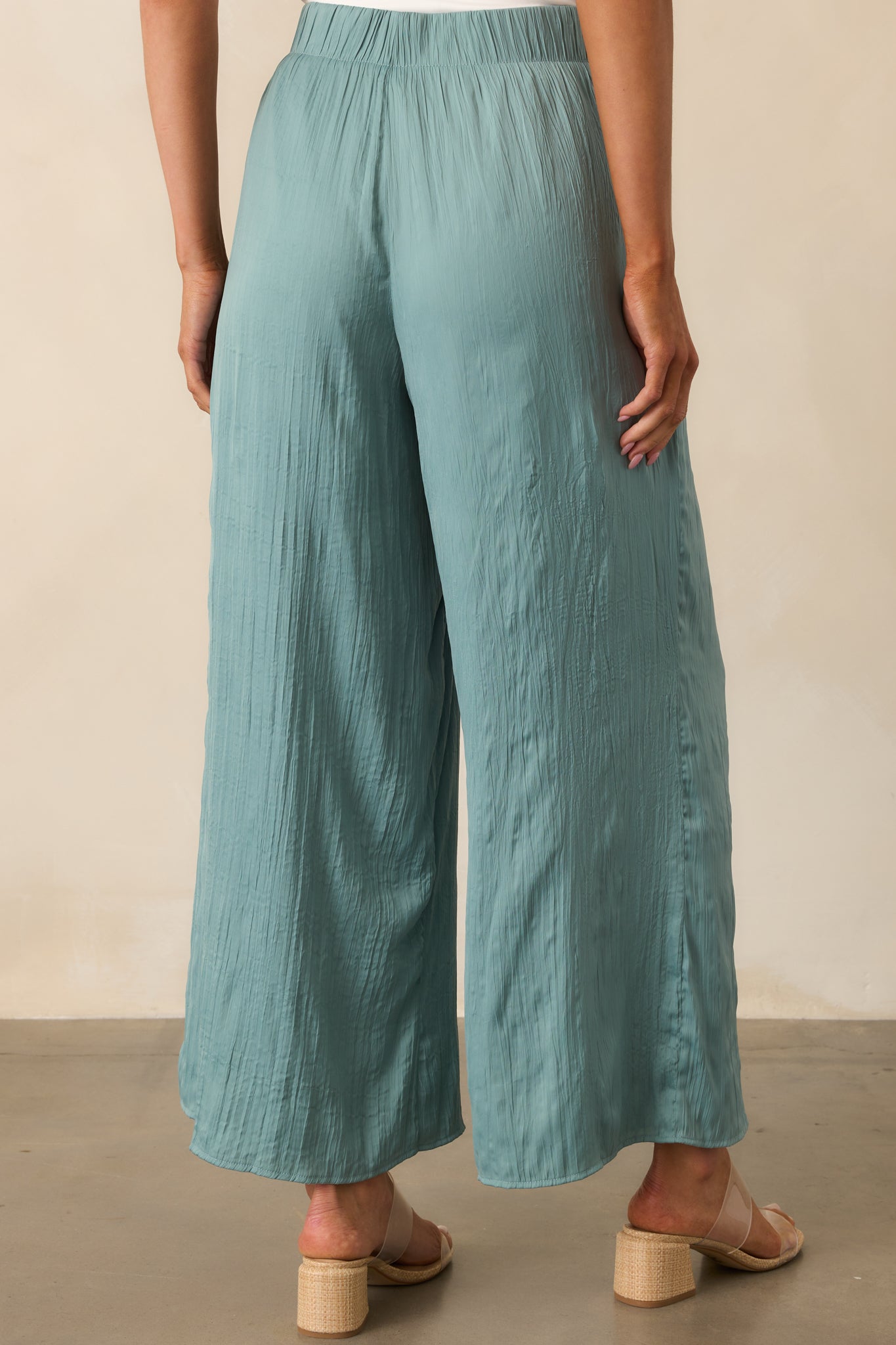 A view from behind showing the elastic waistband and wide leg shape of the sage green satin pants.