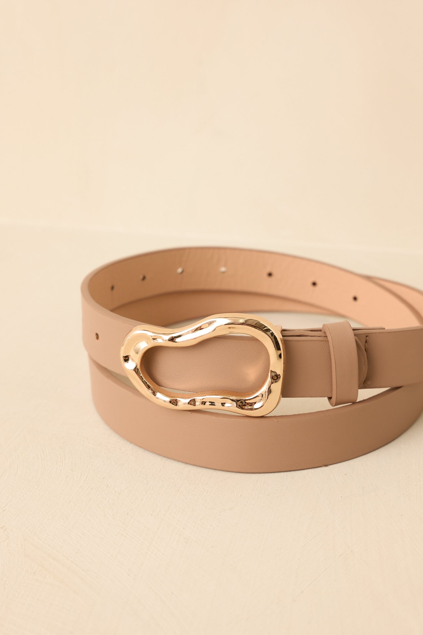Detailed close-up of beige belt showcasing sculptural gold buckle with organic shape and refined faux leather texture.