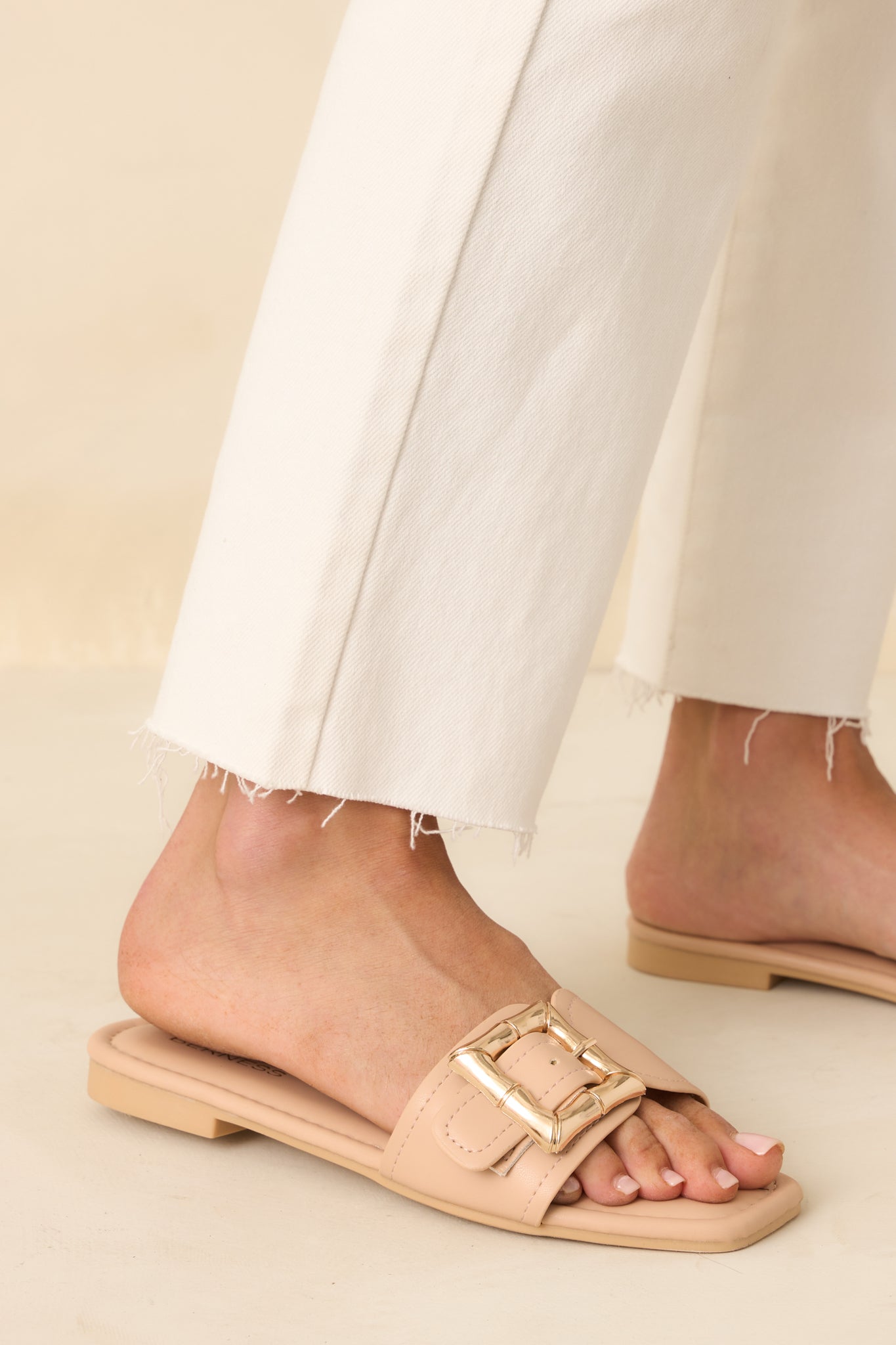Side angle view of the beige sandals showing the slip-on design and gold buckle detail.