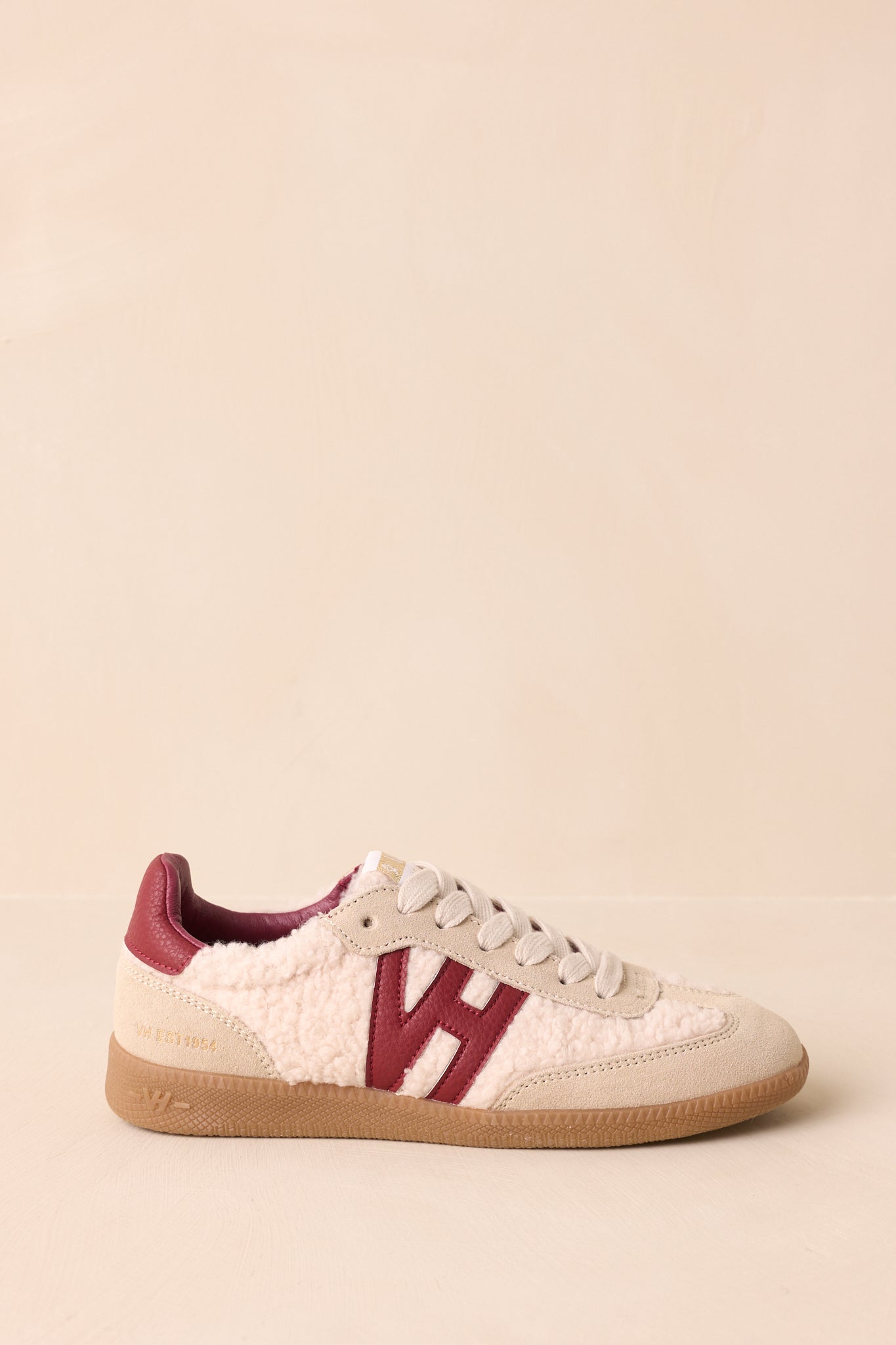 Side view of beige and burgundy low-top sneakers with sherpa and suede panels, lace-up front, and bold side logo patch.