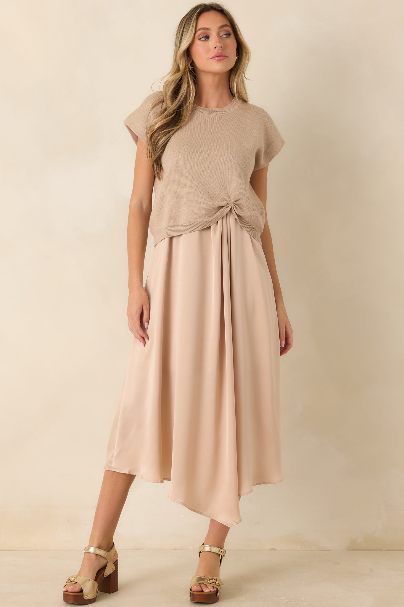 Front view highlighting the cinched front hem, ribbed crew neckline, and relaxed fit of the beige knit sweater.