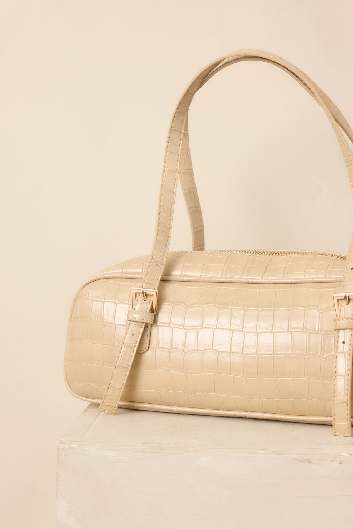 Close-up of the beige handbag’s faux crocodile texture, showcasing the dimensional pattern and smooth zipper closure.