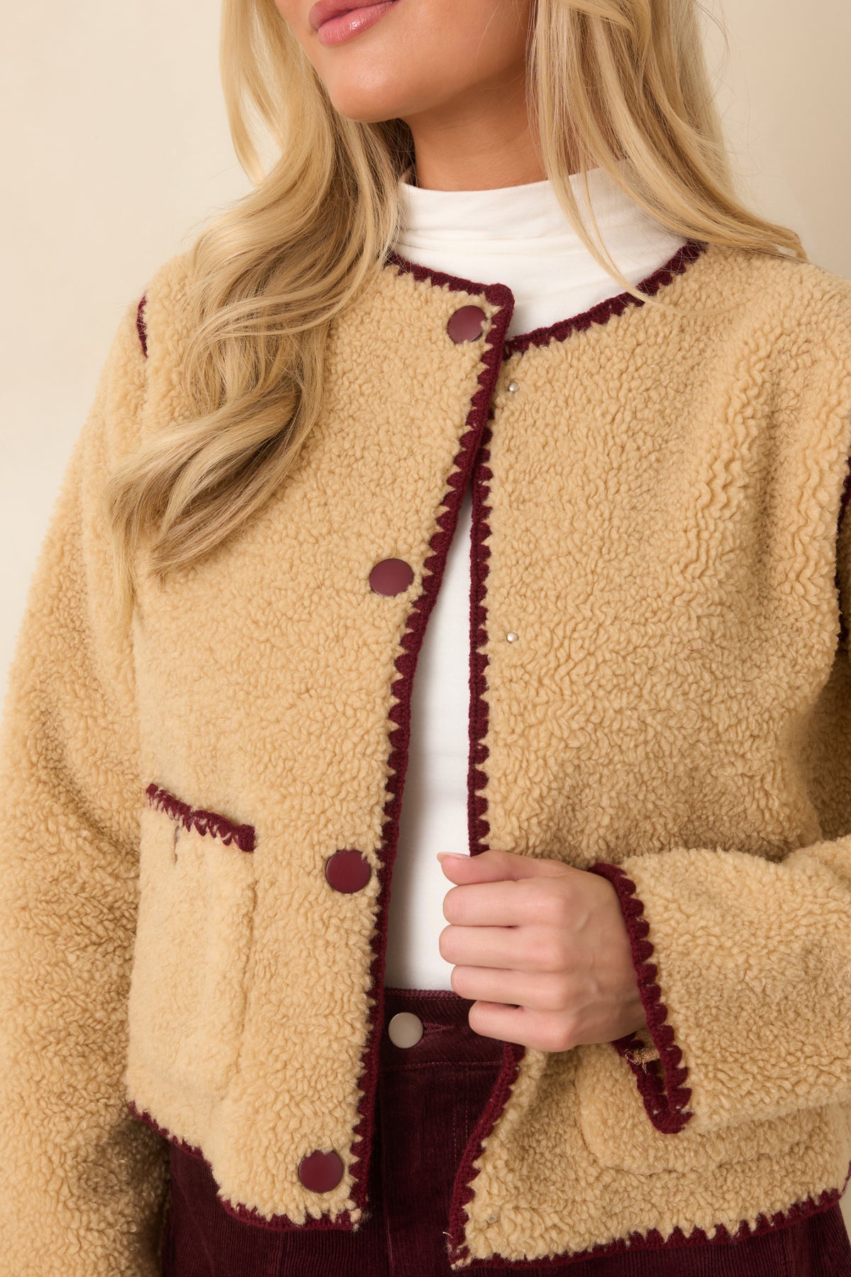 Two front patch pockets add practical detail to the plush beige sherpa jacket.
