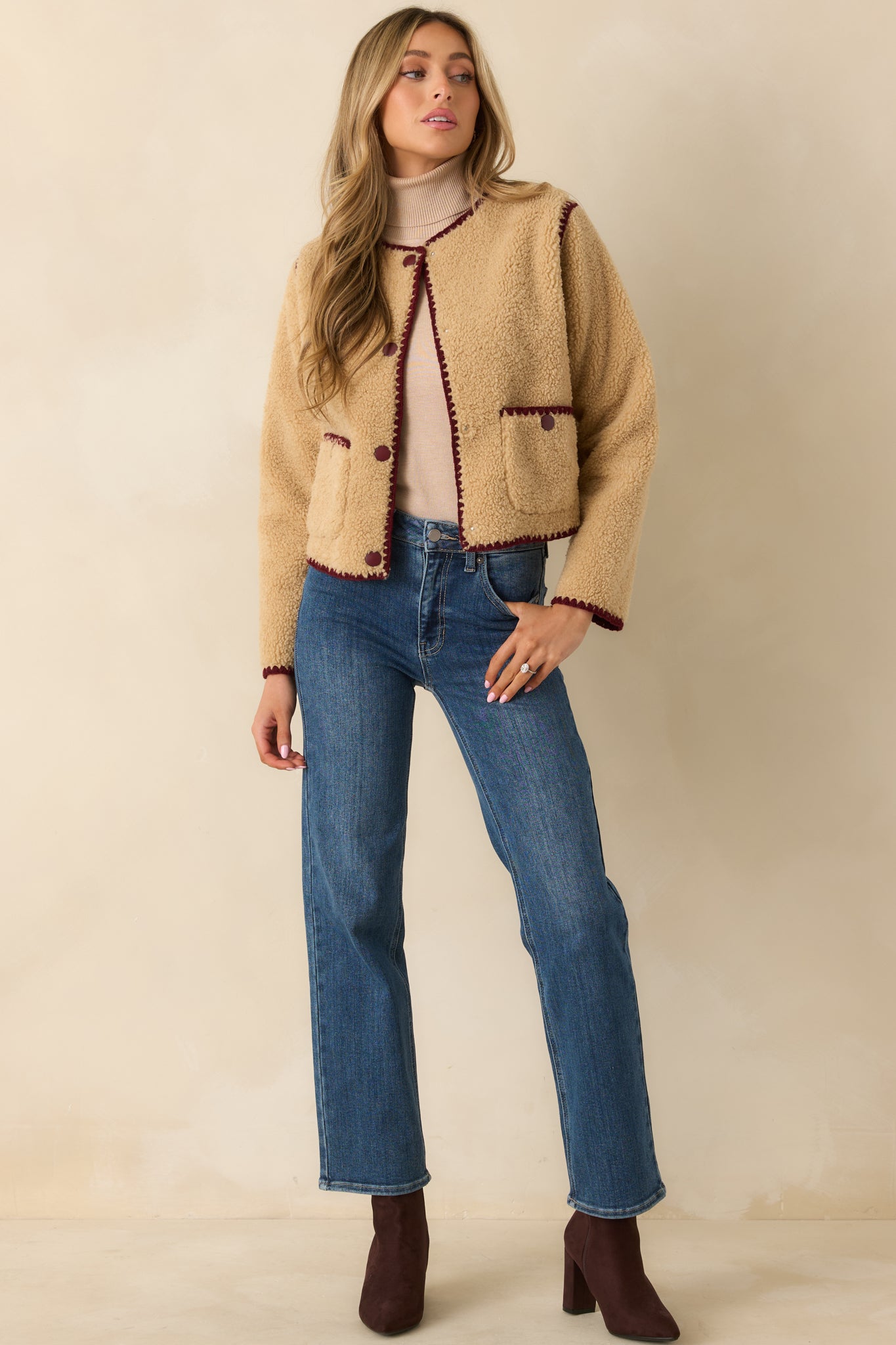Beige faux sherpa jacket showing plush texture and burgundy whipstitch trim.