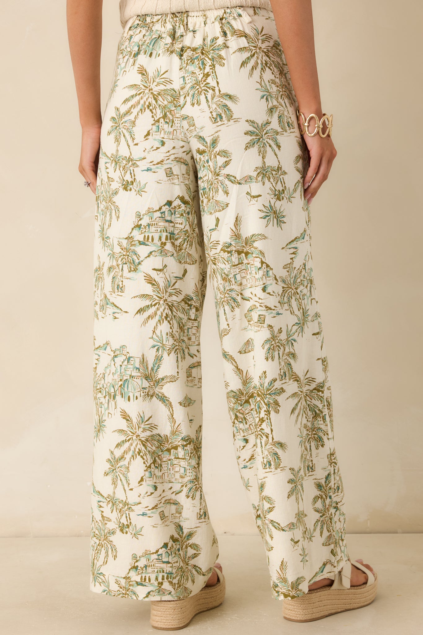 Back view of the beige and green printed pants featuring an elastic waistband, wide leg silhouette, and full-length drape.