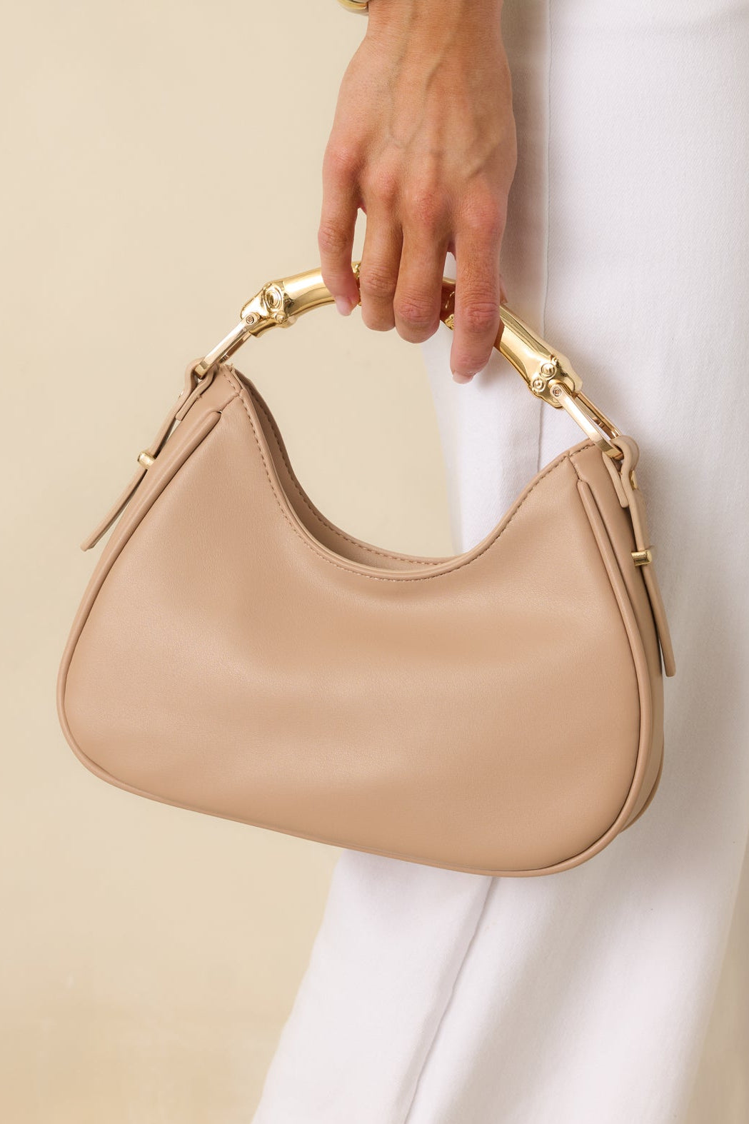 Cropped view of the beige handbag showing the smooth faux leather exterior, structured silhouette, and gold-tone bamboo-inspired top handle.