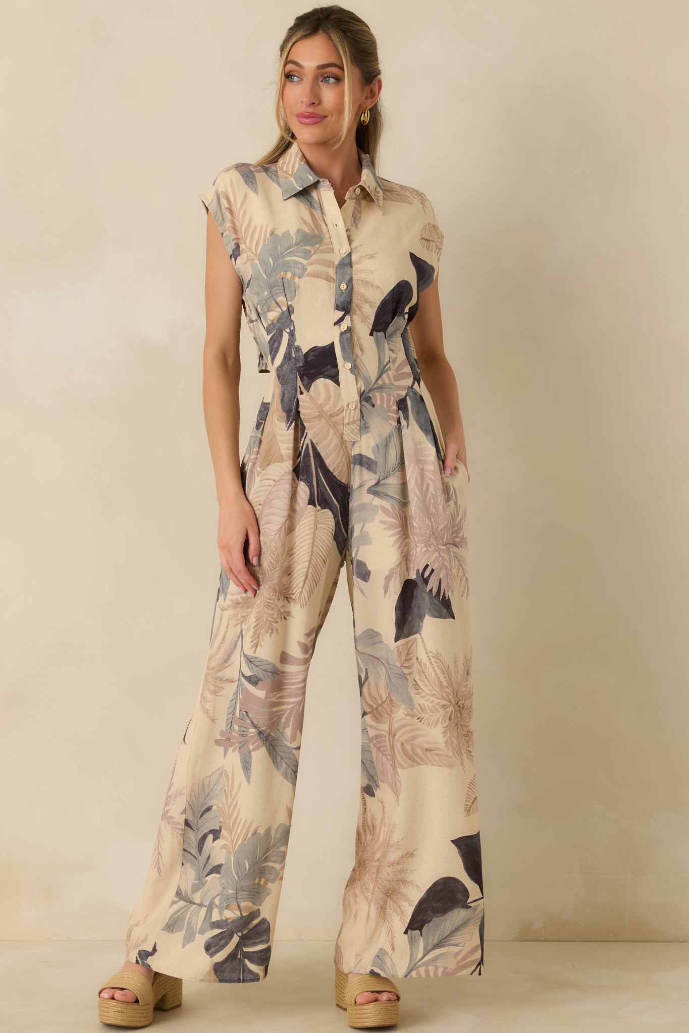 Beige woven jumpsuit with vibrant tropical print, cap sleeves, and lightweight wide-leg design.