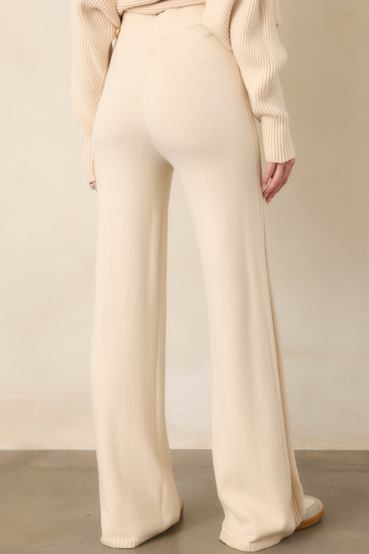 Rear view of the beige knit pants highlighting the smooth fit through the hips, clean seam construction, elastic waistband, and flowing wide-leg shape.