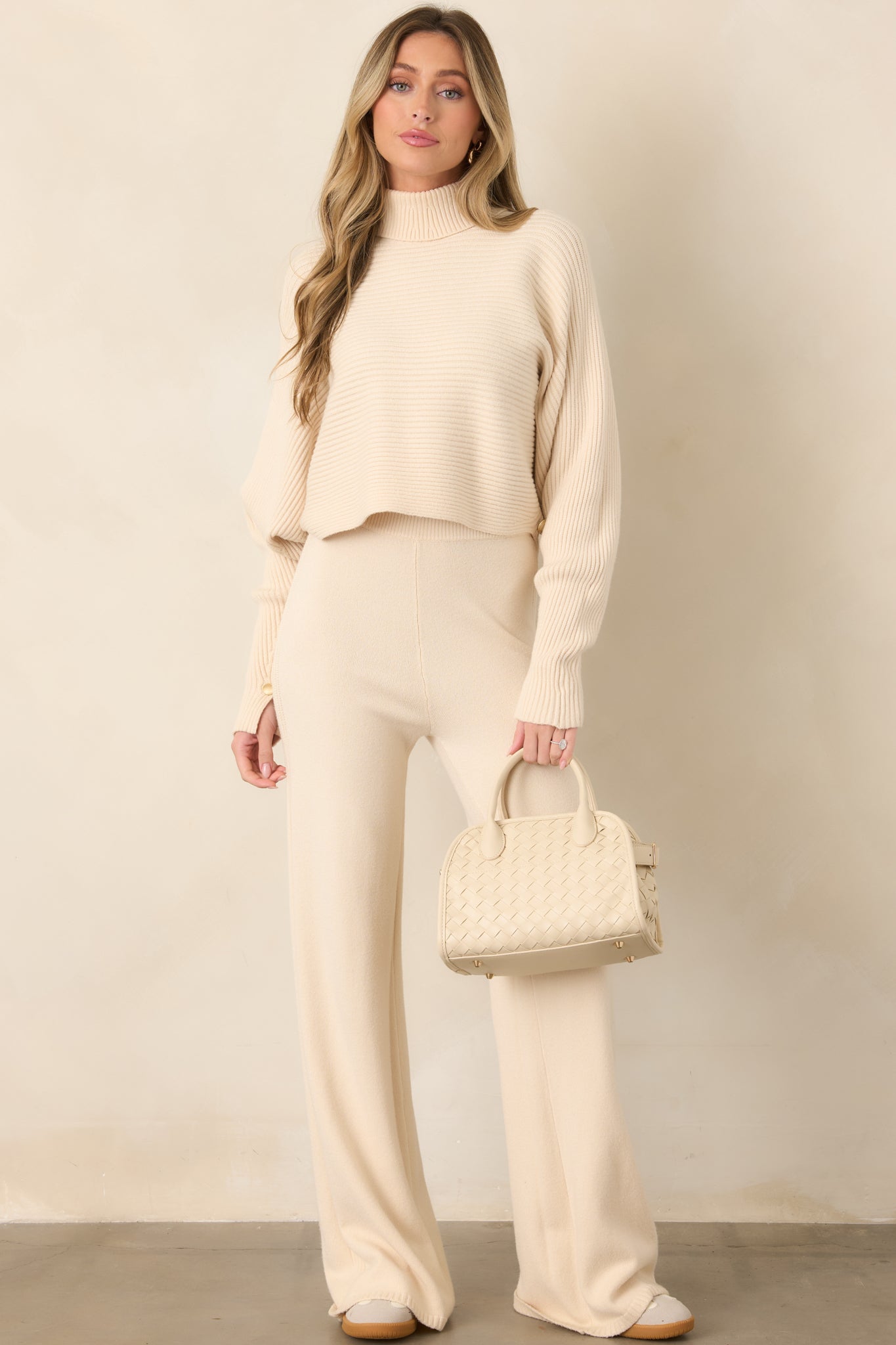 Beige knit pants with a high-rise elastic waistband, smooth hip fit, wide straight legs, and subtle ribbed detailing along the outer sides.