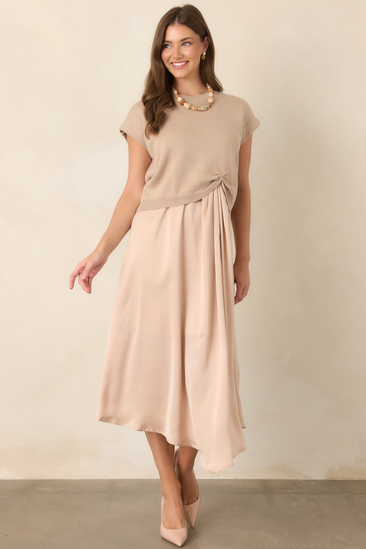 Neutral beige knit sweater featuring a relaxed silhouette, ribbed crew neckline, cap-style sleeves, and cinched front hem detail.