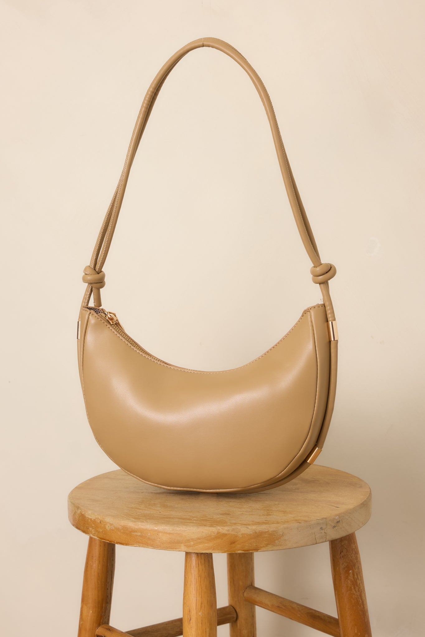 Close view of the beige handbag highlighting the knotted shoulder strap and polished gold-tone accents.