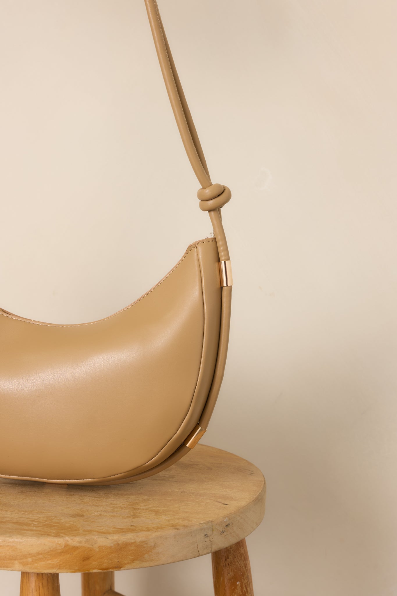 Close-up of the handbag's knotted strap, polished gold-tone hardware, and smooth neutral beige finish.