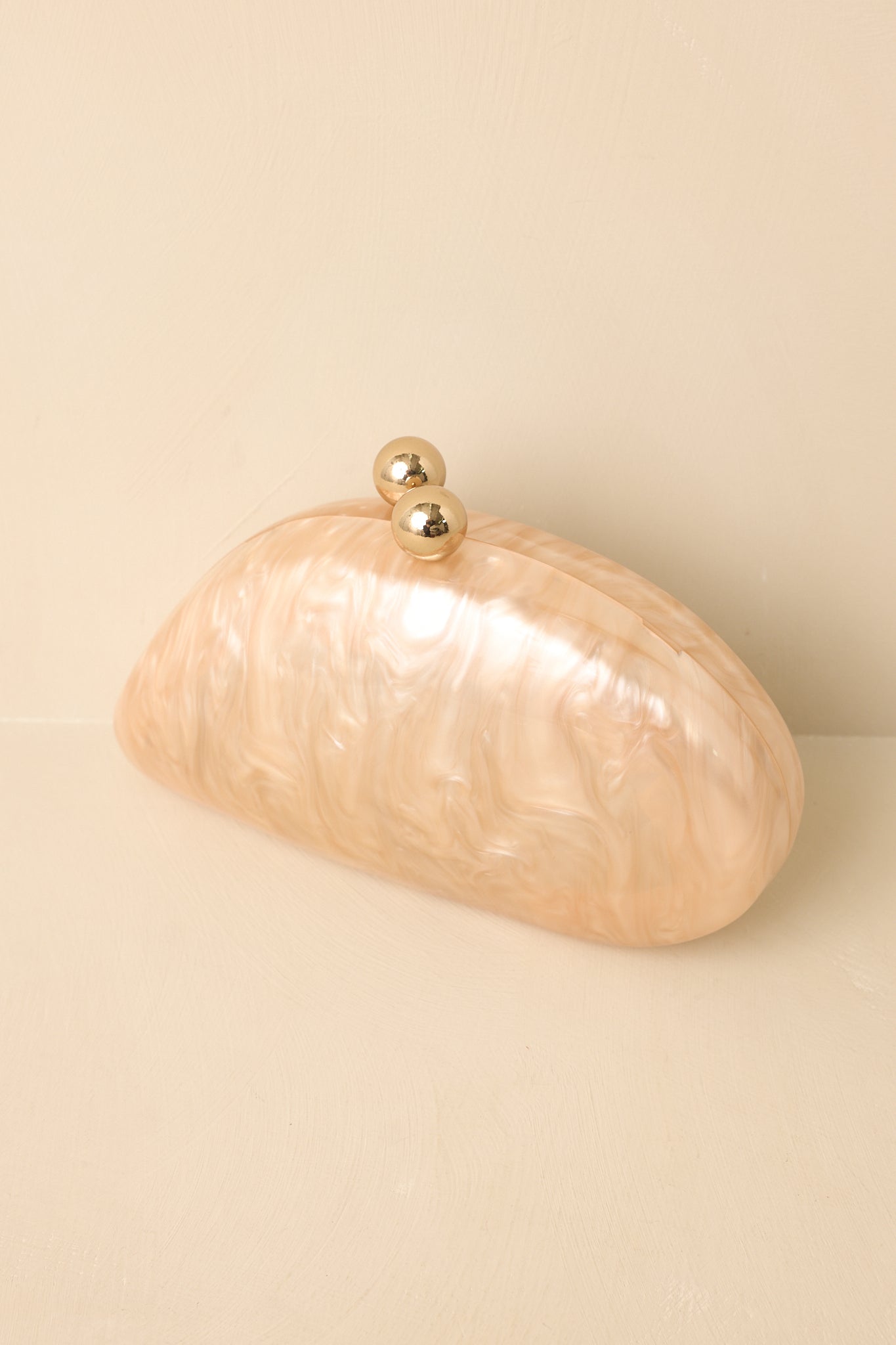 Beige marble clutch highlighting the smooth textured exterior, oval shape, gold hardware, and elegant silhouette.