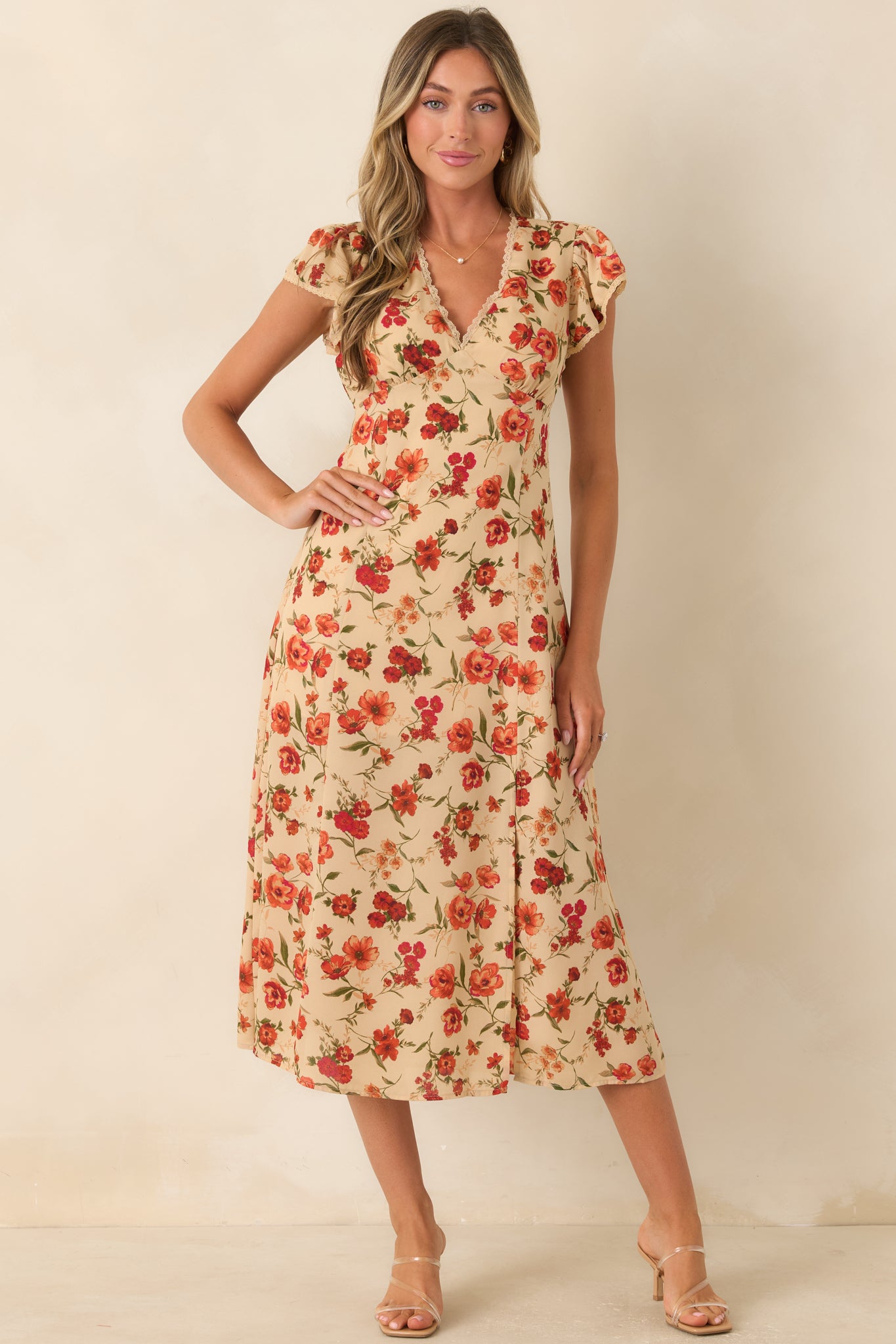 Light beige midi dress with a red, coral, and green floral print, fitted waist, flowing skirt, and airy side slit.