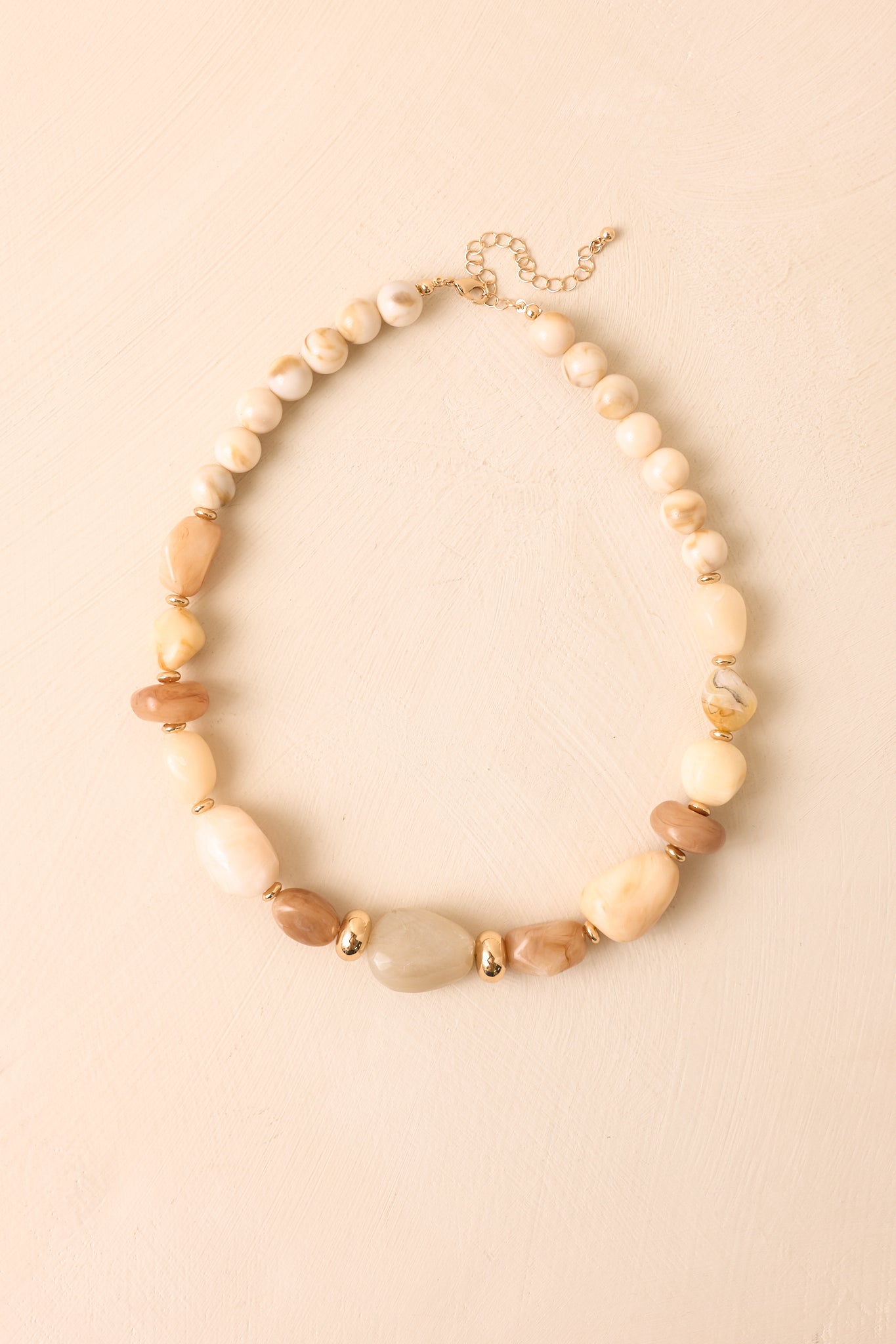 Beige mixed bead necklace displayed against a beige background, highlighting ivory, caramel, and marbled resin beads with gold-tone accents.