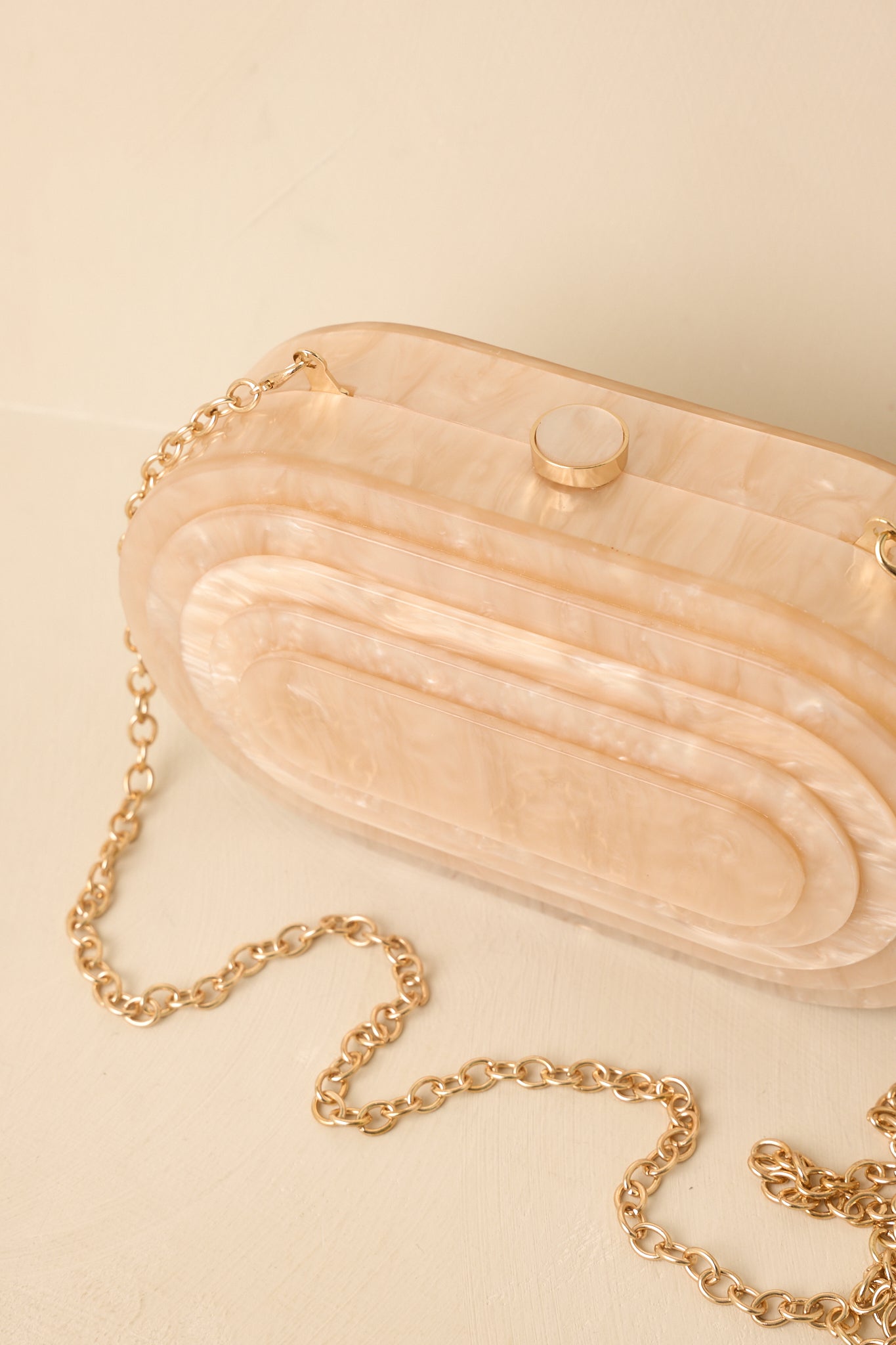 Beige oval clutch highlighting the luminous finish, structured shape, top clasp, and refined details.