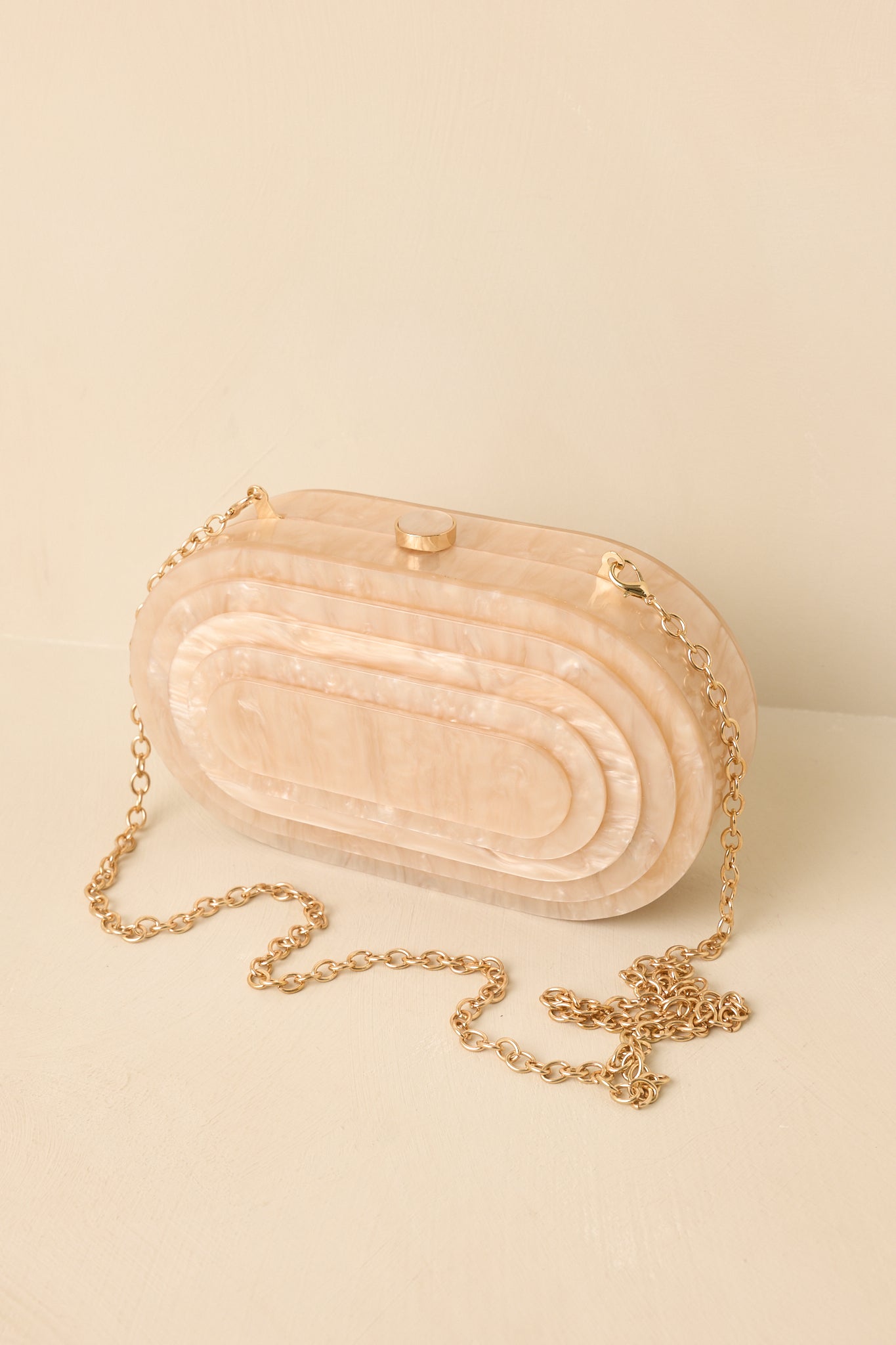 Beige pearlescent clutch featuring a structured oval silhouette, luminous finish, top clasp closure, and chain strap.