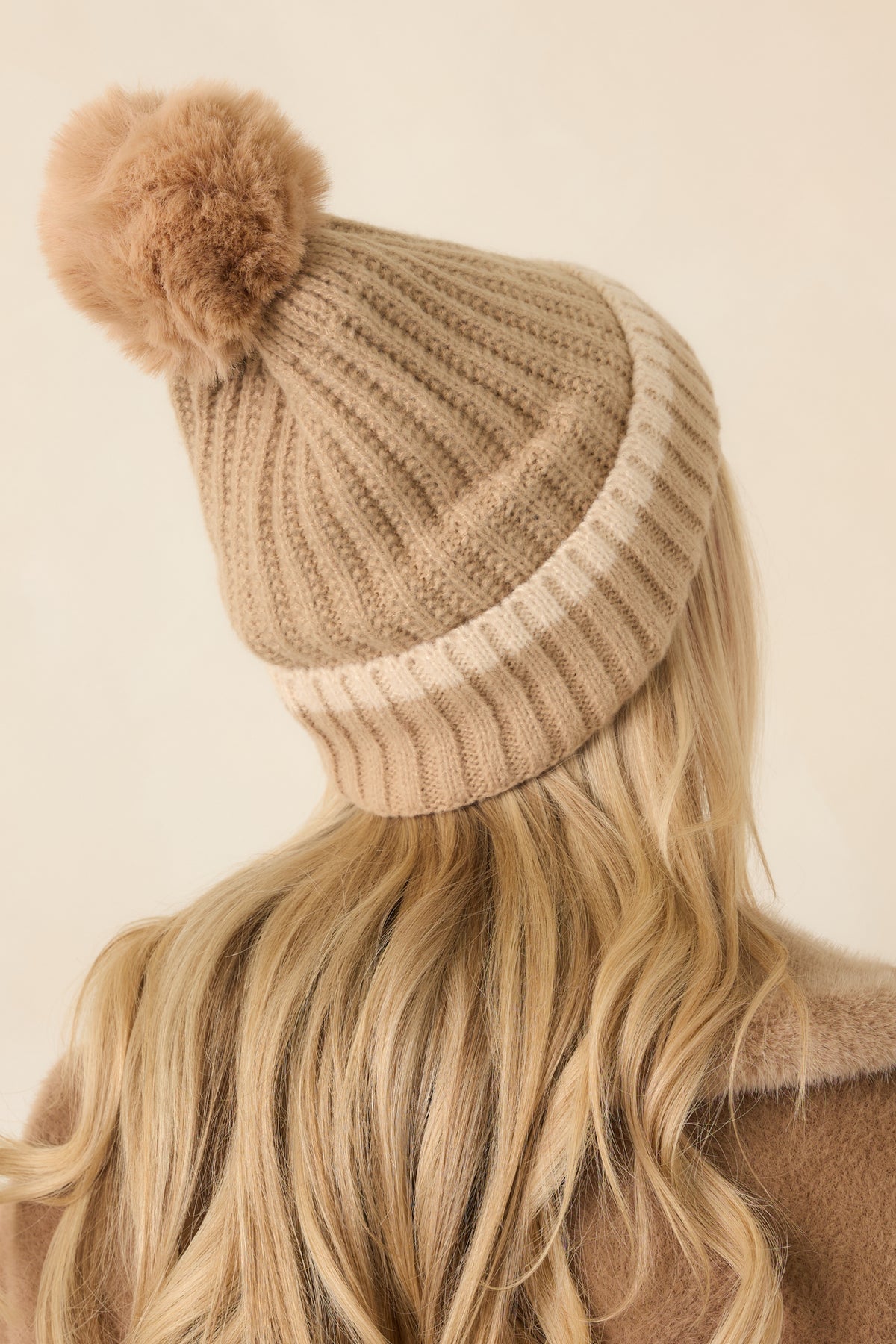 Rear view of the beige knit hat showcases its vertical ribbing, relaxed slouchy crown, and wide fold-over cuff.