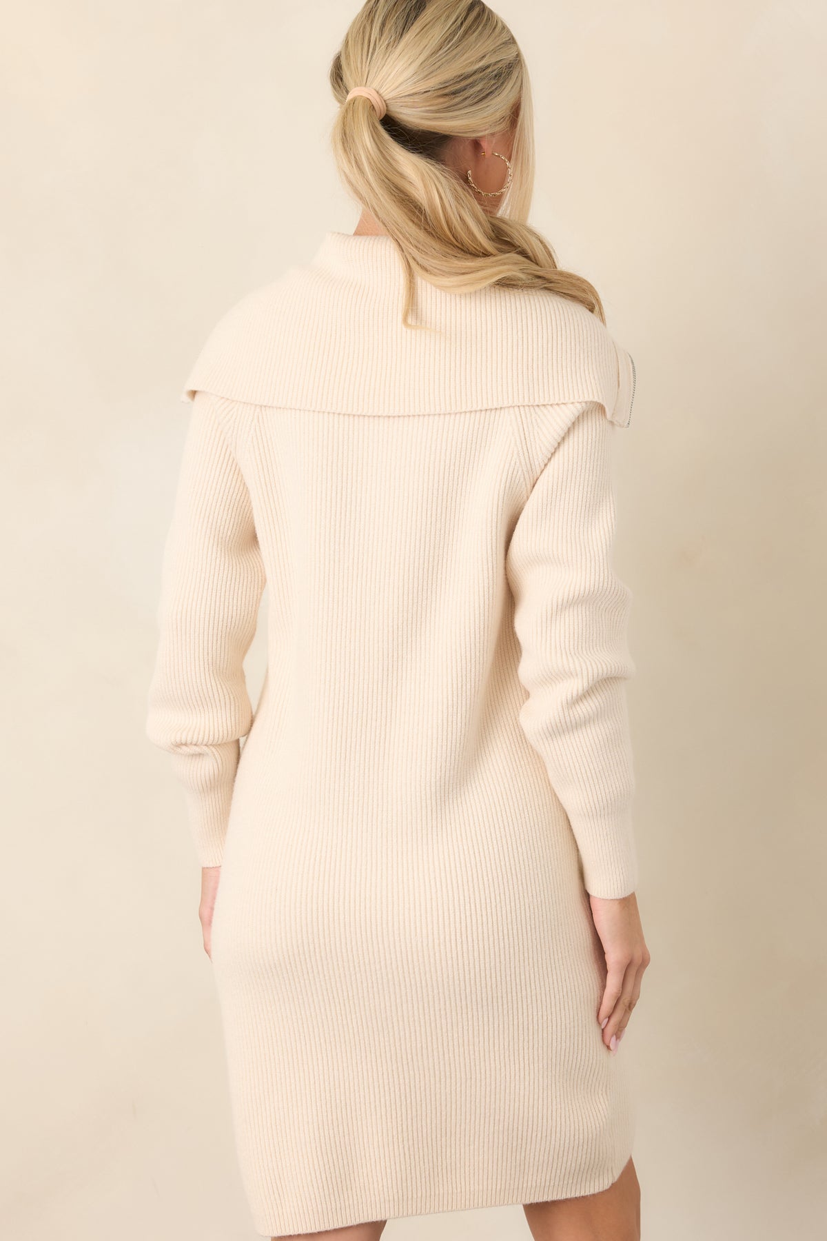 Rear view of the beige sweater dress showcasing its relaxed longline silhouette, vertical ribbed texture, long sleeves, and straight hem.
