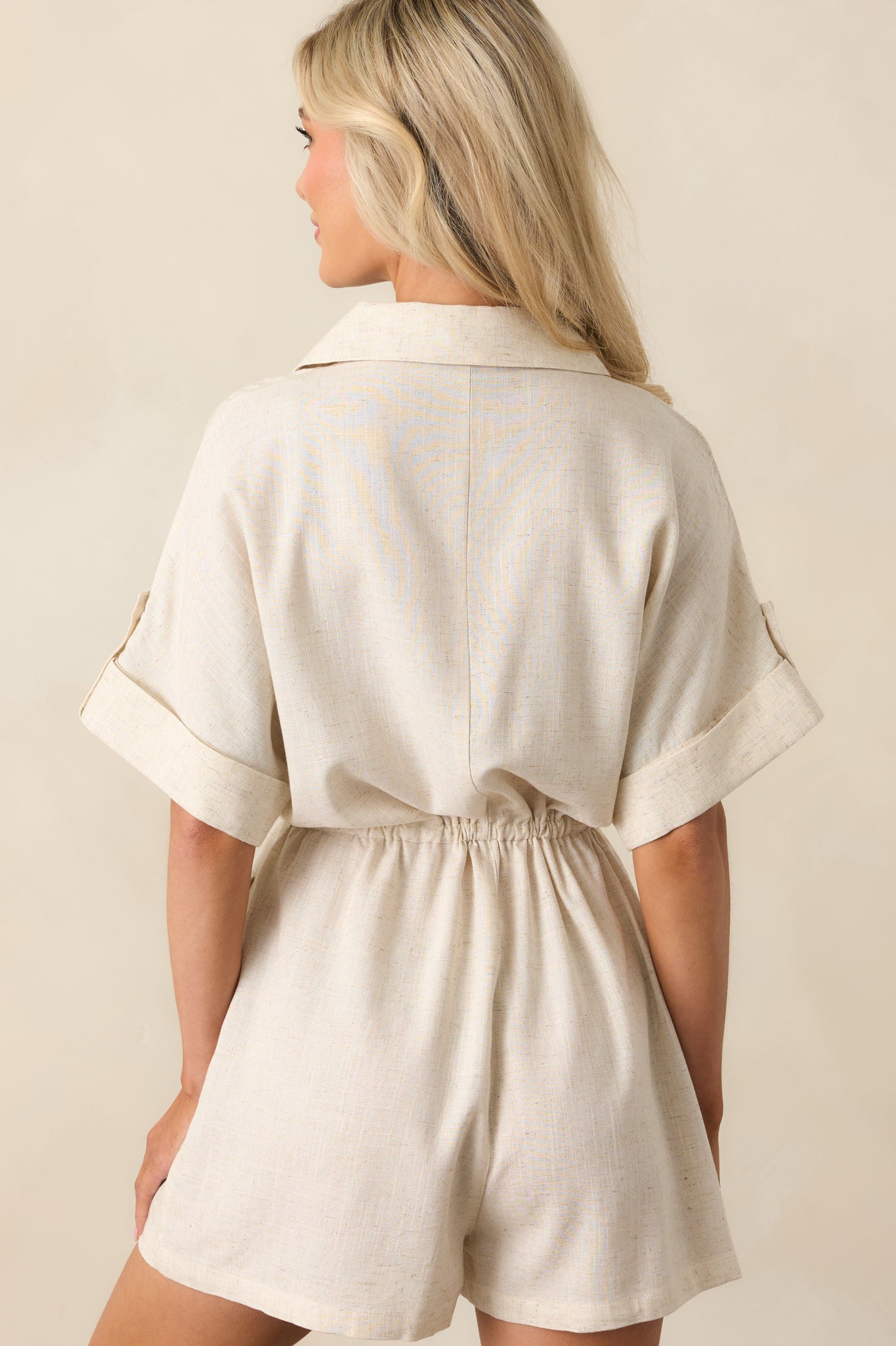 Rear view of the beige romper showing the straight back seam, relaxed silhouette, and rear pocket detailing.