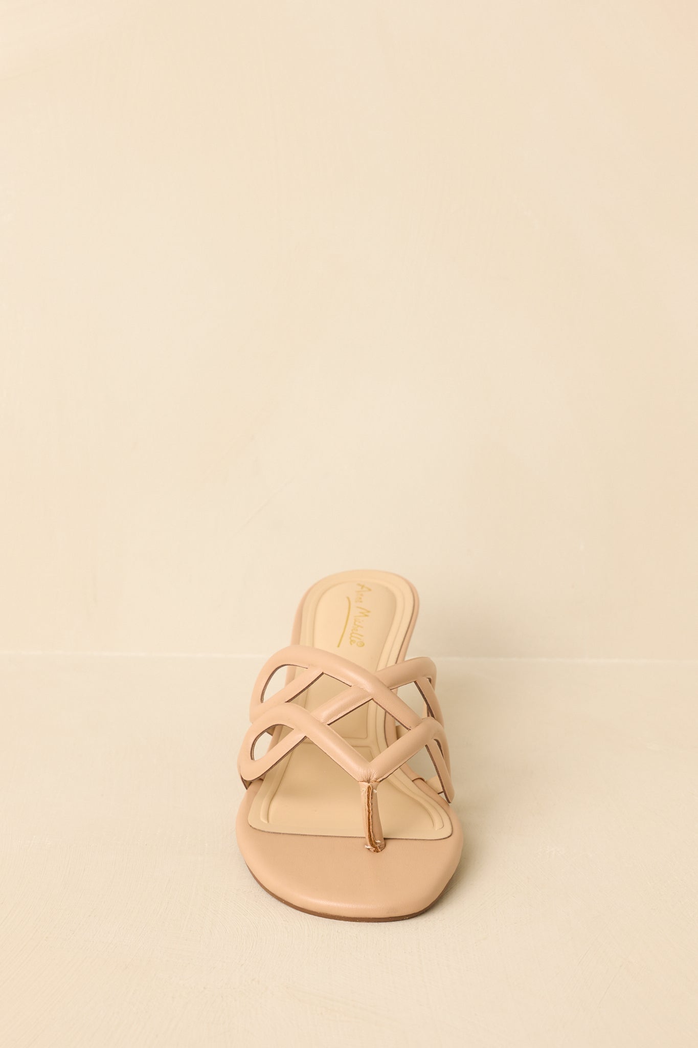 Front view of beige sandals displaying open toe and sculptural strap detail.