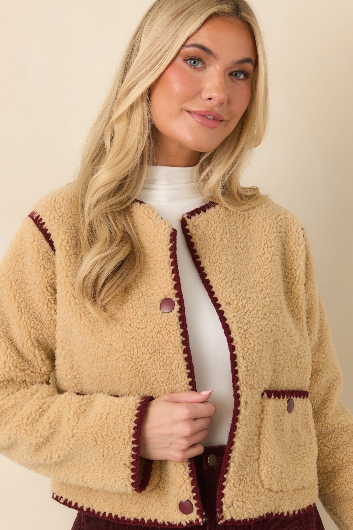 Long beige sherpa sleeves feature a soft plush texture and burgundy whipstitch detailing along the edges.