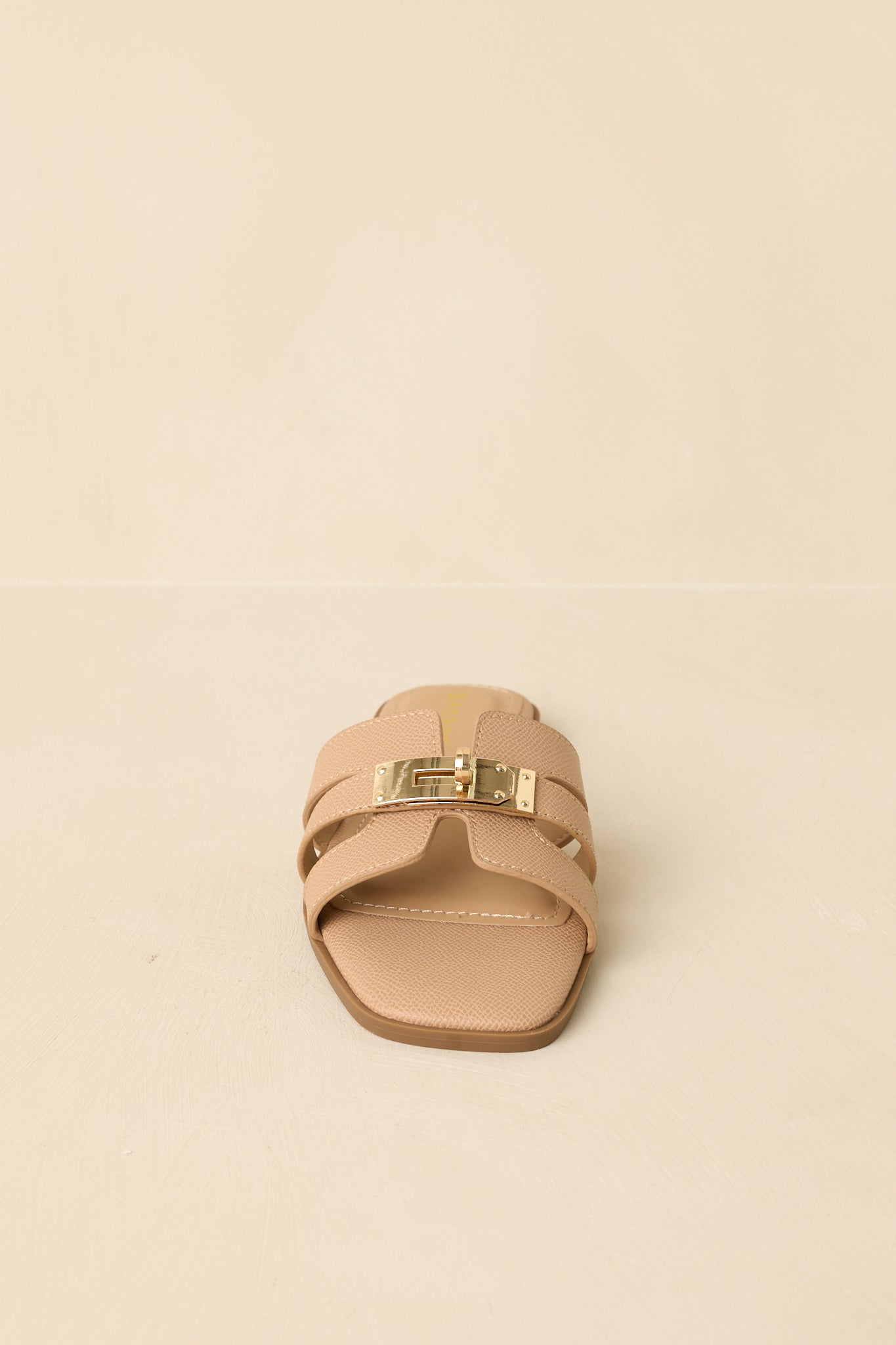 Straight on shot of beige slide sandals highlighting textured faux leather straps and gold-tone hardware detail.