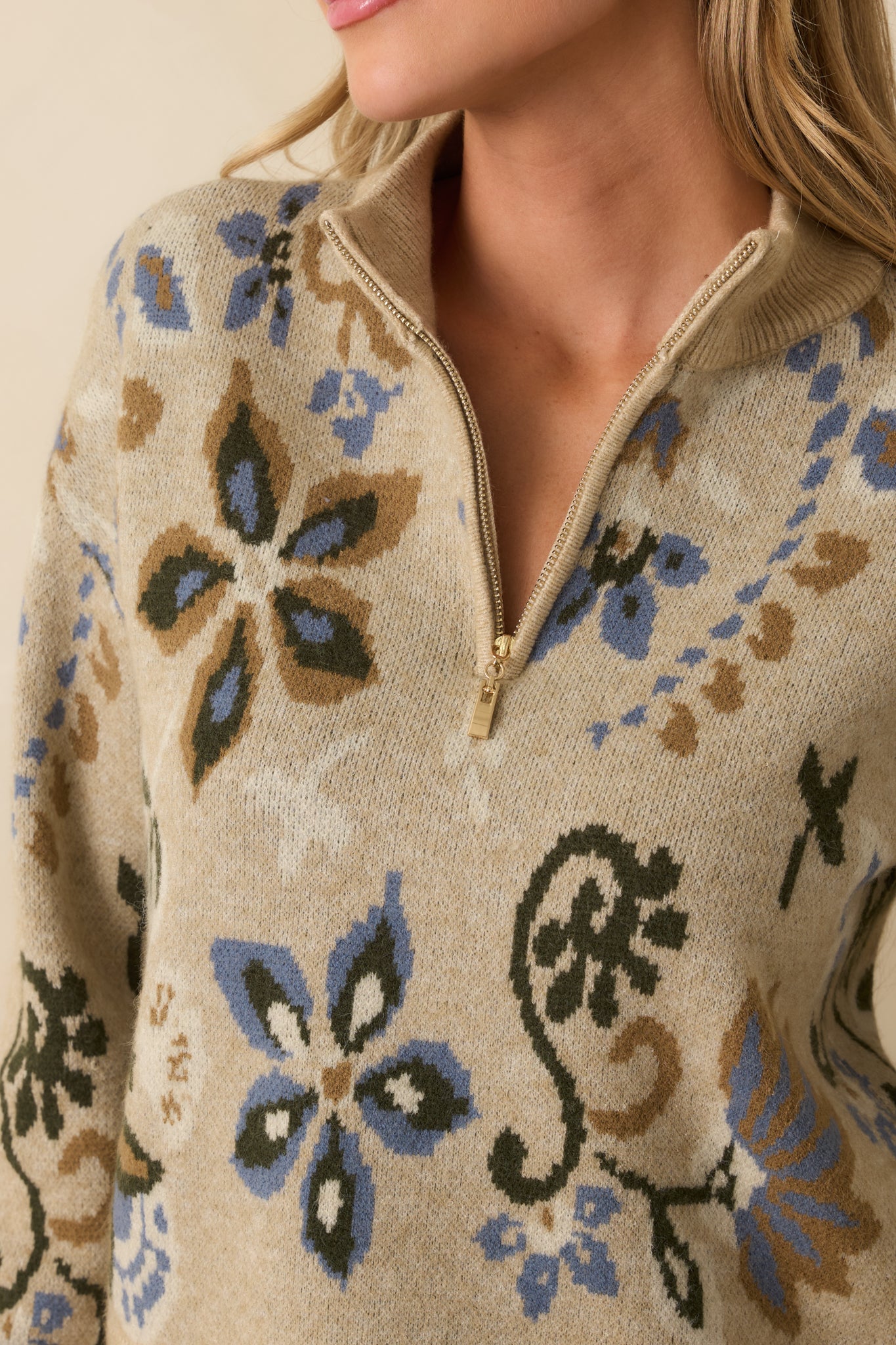Tight detail of the beige knit fabric showing the blue multicolor floral design and half-zip closure.