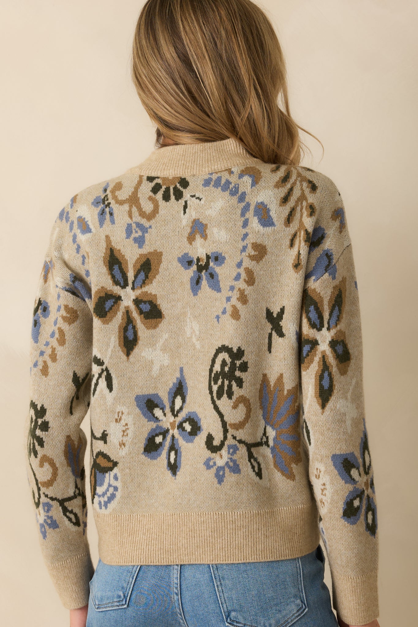 Rear view of the beige sweater with smooth knit back and long sleeves with ribbed cuffs.