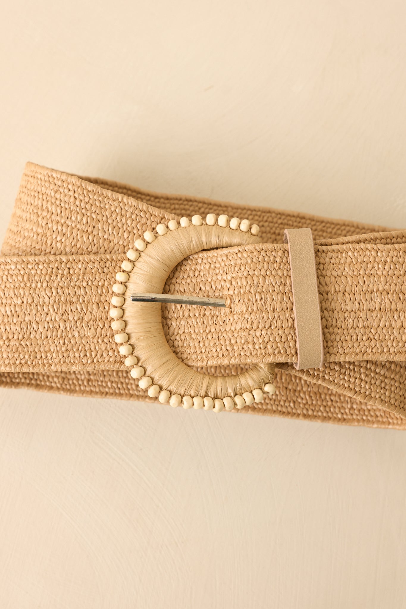 Beige woven belt with a decorative buckle on a beige background